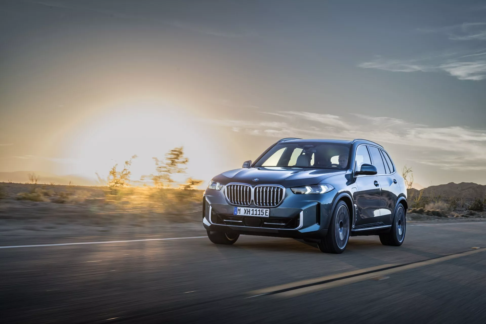 BMW X5 2023 (G05-F95 Facelift) v pohybe: Dynamický pohľad z nízkeho uhla zdôrazňujúci LED svetlomety, zliatinové kolesá a aerodynamický dizajn na pozadí západu slnka