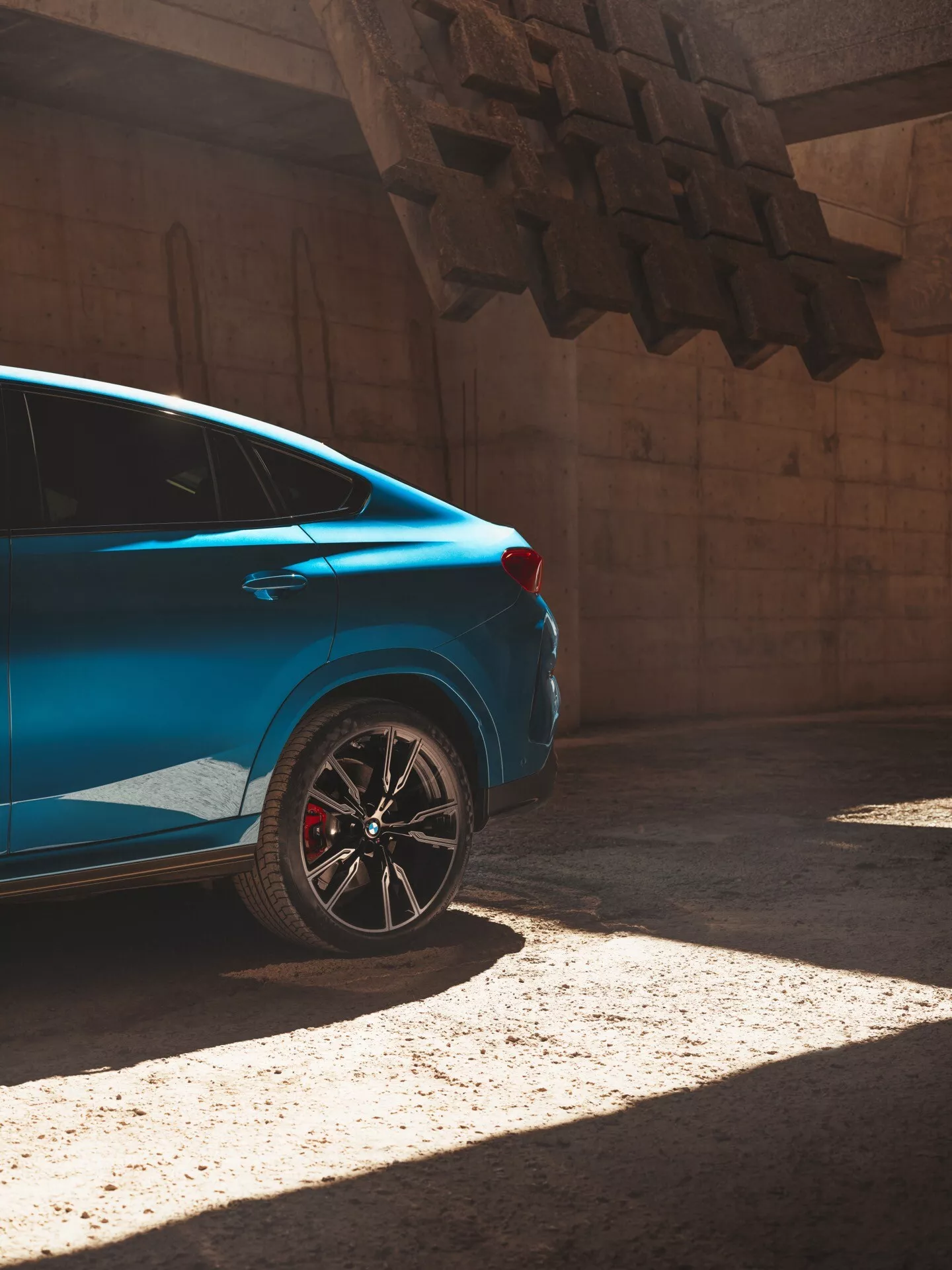 Modré auto BMW X6 2023 (G06/F96 facelift) na slnku, zobrazené z trojštvrťovej zadnej perspektívy zdôrazňujúcej zadnú štvrtinu so športovým ráfikom a červeným brzdovým strmcom.