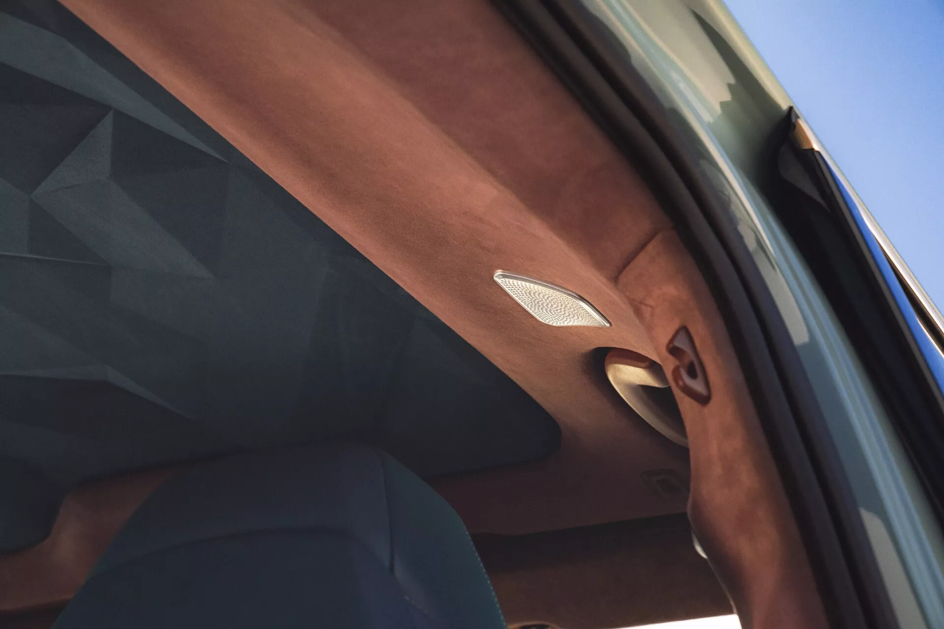 Detailný pohľad dovnútra BMW XM 2023, zameriavajúci sa na vysoko detailný bočný stĺp na strane spolujazdca s prémiovým mriežkou reproduktora s kovovou obrubou a zložitými textúrnymi detailmi, naznačujúcimi luxusný interiérový dizajn.