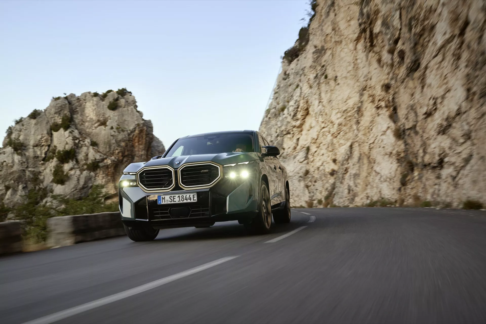 Dynamický predný trojštvrťový pohľad na BMW XM (G09) 2023 na kľukatej horskej ceste, zobrazujúci moderné LED svetlomety, veľkú mriežku, aerodynamický dizajn a pokročilé technologické funkcie.