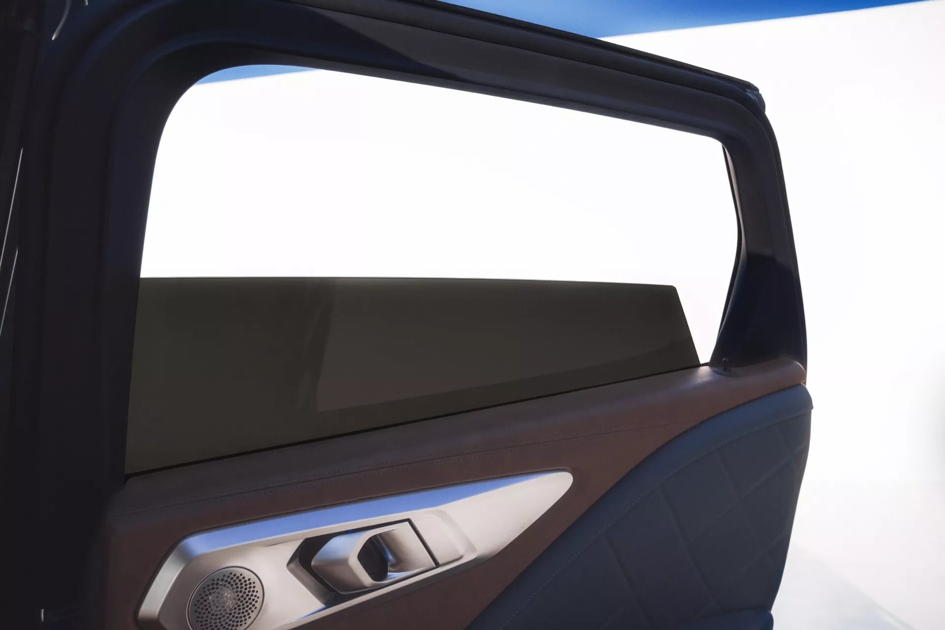 Detailný interiérový pohľad na BMW XM (G09) z roku 2023 s prémiovým okrajom okna, dvojfarebným panelom dverí s možným dreveným obkladom a koženkou, modernou mriežkou reproduktora, kovovou kľučkou a ovládacími prvkami a ambientným osvetlením, zdôrazňujúci luxus a dizajnové detaily.