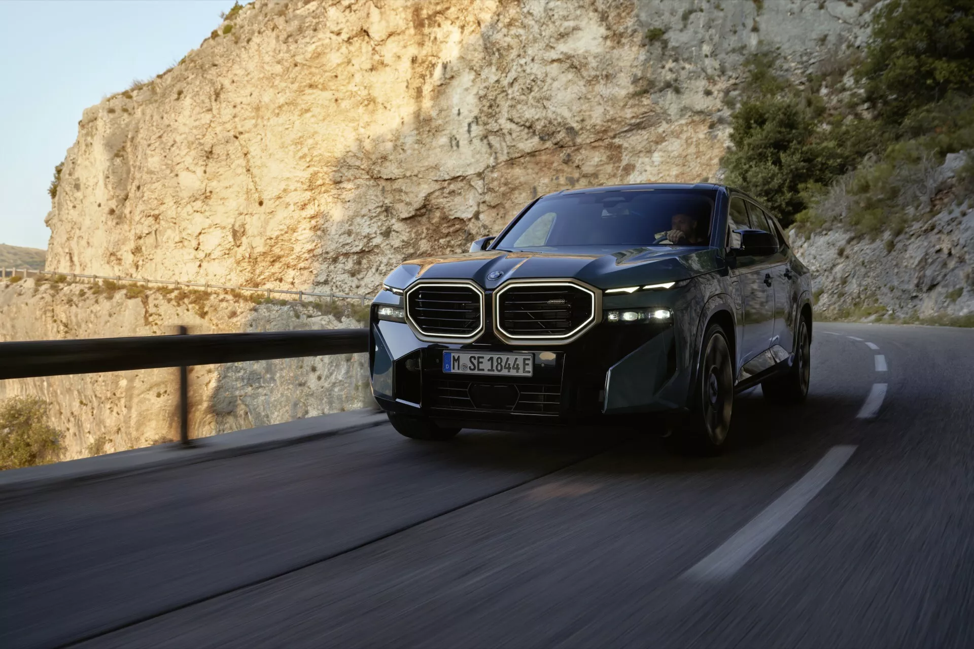 BMW XM (G09) 2023 v pohybe na kľukatej horskej ceste, ktoré predvádza svoj dynamický dizajn a pokročilé technologické funkcie, ako sú ikonická obličkovitá mriežka, LED svetlomety a zliatinové kolesá