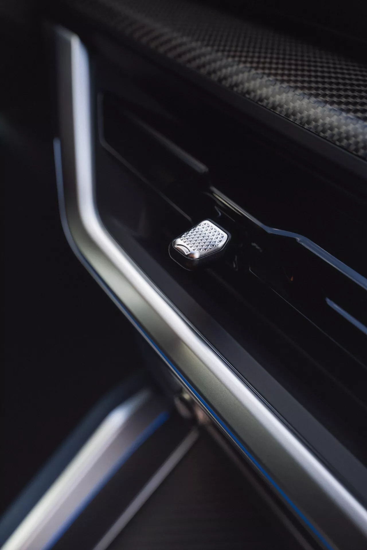 Detailný pohľad na kovové tlačidlo s vysokou textúrou vo dverách interiéru BMW XM (G09) z roku 2023, s malou hĺbkou ostrosti zdôrazňujúcou jeho dizajn a okolité luxusné materiály