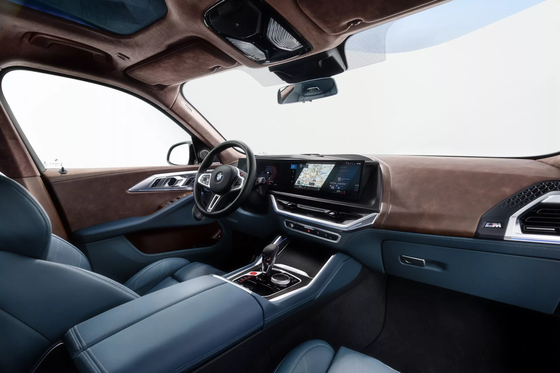 Detailný pohľad na interiér BMW XM (G09) z roku 2023, zobrazujúci vodičové sedadlo, modernú prístrojovú dosku s digitálnymi ukazovateľmi, dotykovú obrazovku infotainmentu a luxusnú stredovú konzolu z perspektívy zadného sedadla