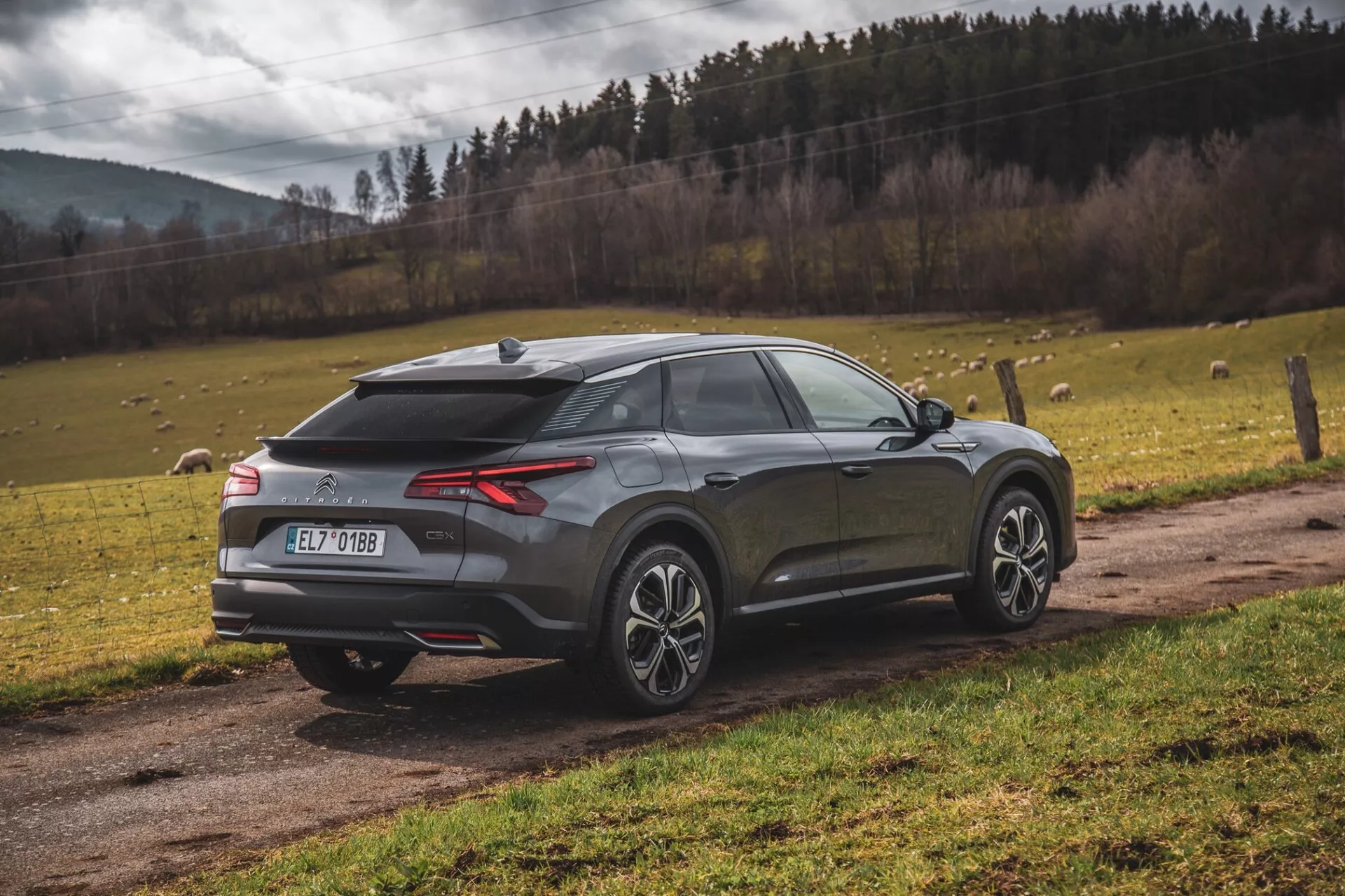 Moderné crossover SUV Citroen C5-X 2022 zaparkované vonku, zobrazenie z troch štvrtín zdôrazňujúce LED zadné svetlá, zadný difúzor, senzory parkovania alebo kameru, anténu v tvare plutvy žraloka, dvojfarebné zliatinové kolesá, sklonené zadné okno, integrovaný spoiler a metalický povrch na pozadí prírodnej krajiny