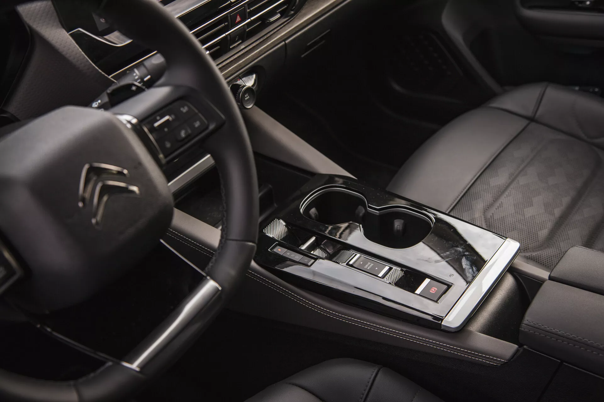 Interiér Citroën C5-X 2022 s multifunkčným volantom s logom, high-tech palubnou doskou s infotainment systémom, elegantnou automatickou radicou pákou, ovládaním klimatizácie, sedadlami potiahnutými kožou s kvalitným prešívaním a nádychom životného štýlu s okuliarmi na lesklej stredovej ploche