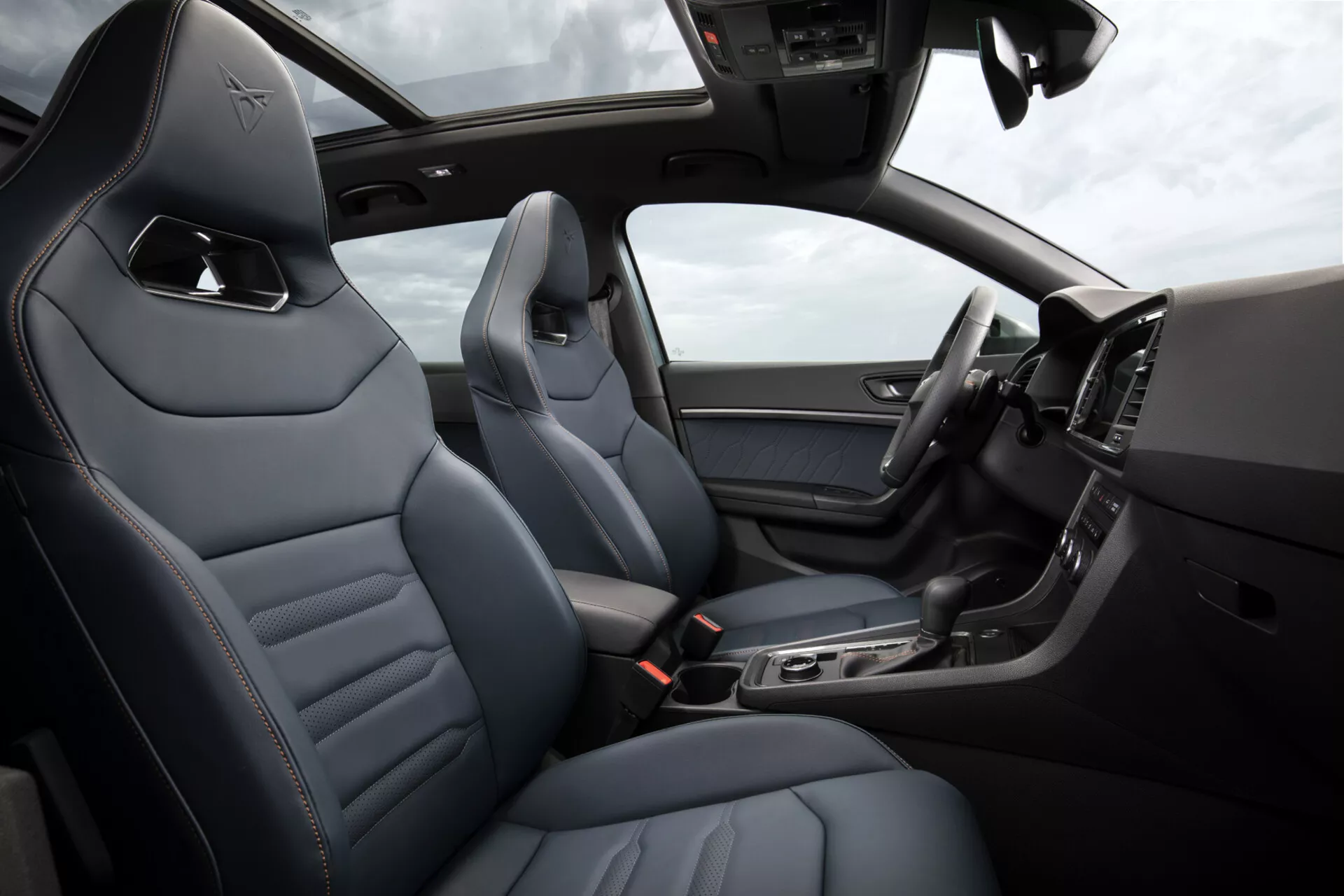 Interiér Cupra Ateca 2020, zobrazujúci luxusné kožené sedadlá s diamantovým prešívaním, štíhlú stredovú konzolu s technologickými funkciami, digitálny displej prístrojovej dosky a časť volantu s ovládačmi, pod osvetlenou strešnou oknou