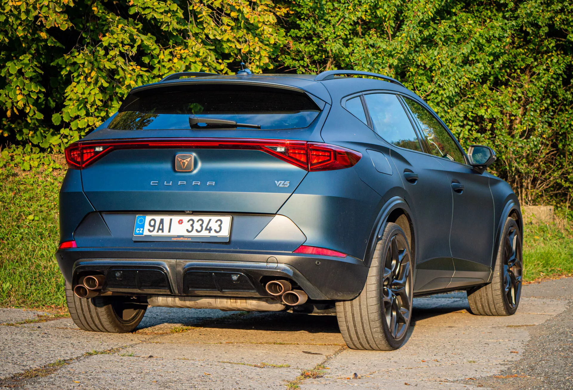 Zadný trojštvrťový pohľad na Cupra Formentor 2020, ktorý zdôrazňuje športové prvky ako sú dvojité výfukové koncovky, spoiler na streche a zliatinové disky, spolu s označením výrobcu a modelu počas dňa