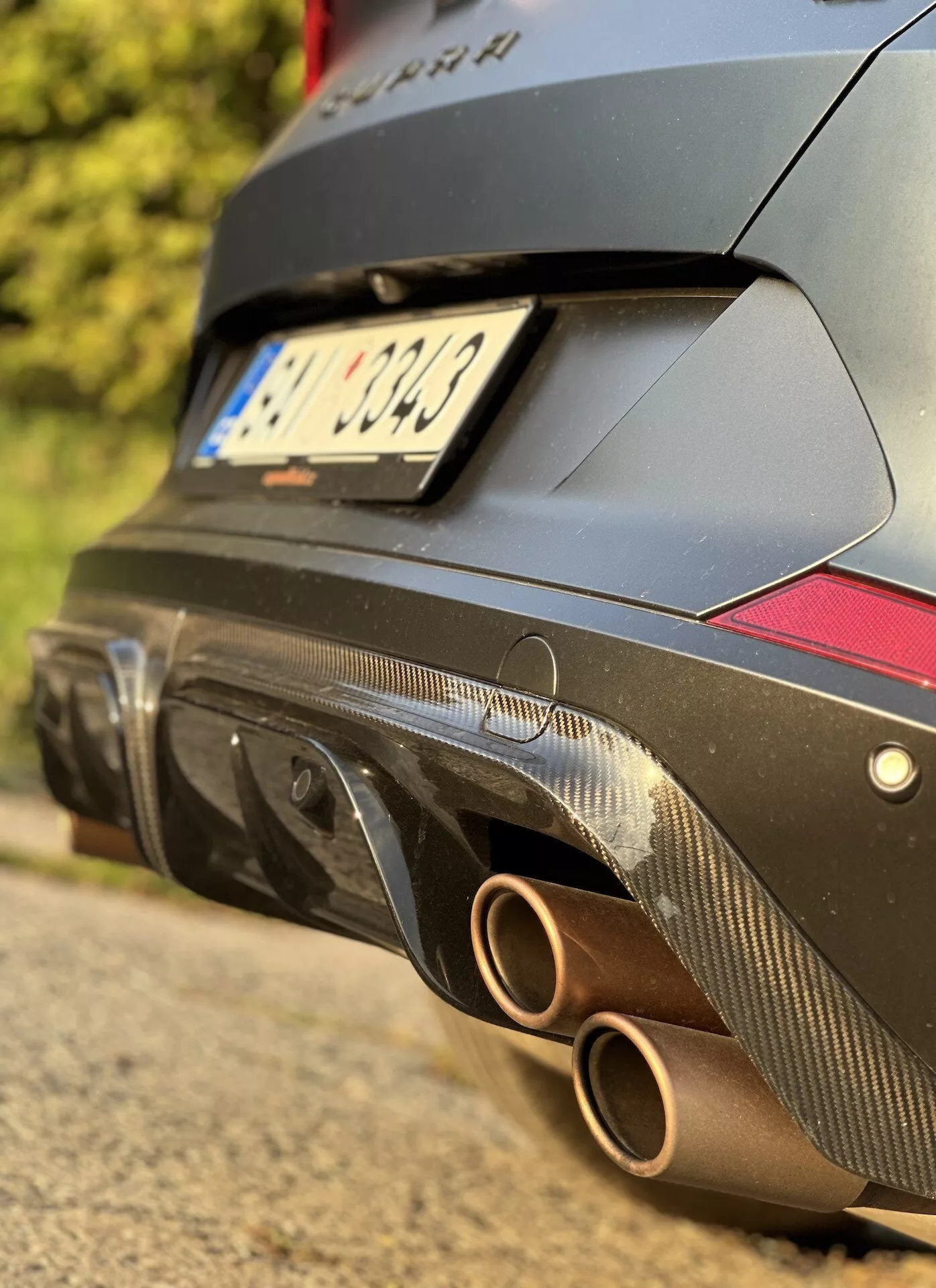 Detailný pohľad na zadnú časť vozidla Cupra Formentor 2020 s dôrazom na dvojitý kruhový výfukový systém a difúzor z uhlíkových vlákien s červenými odrazičmi na pozadí tmavo farbeného tela orientovaného na výkon.