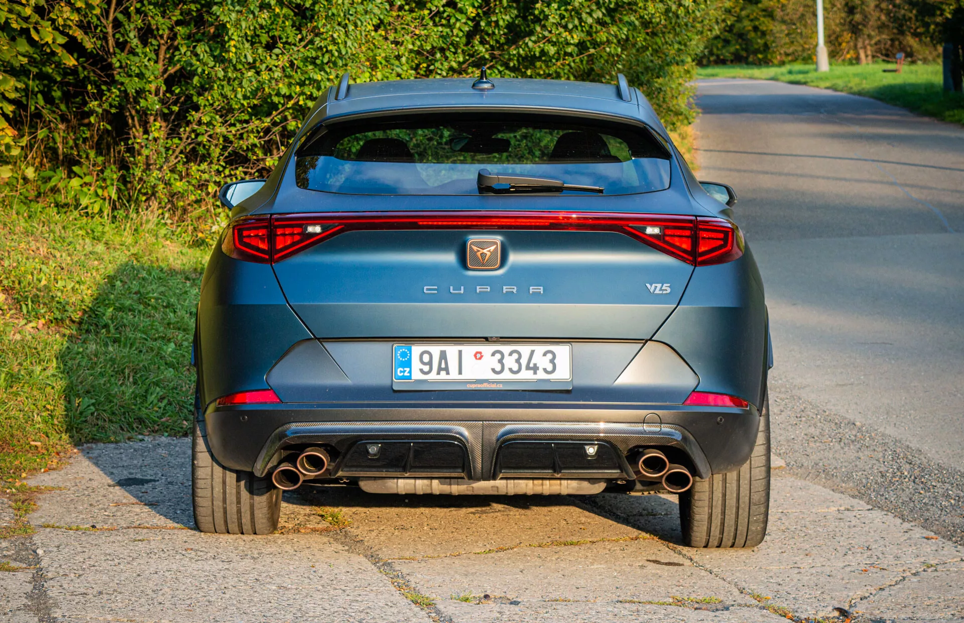 Zadný pohľad na metalický šedý CUPRA Formentor VZ5 z roku 2020 zaparkovaný na okraji cesty, zobrazujúci LED zadné svetlá, dvojité výfuky a aerodynamické dizajnové prvky počas záberu v svetle neskorého popoludnia