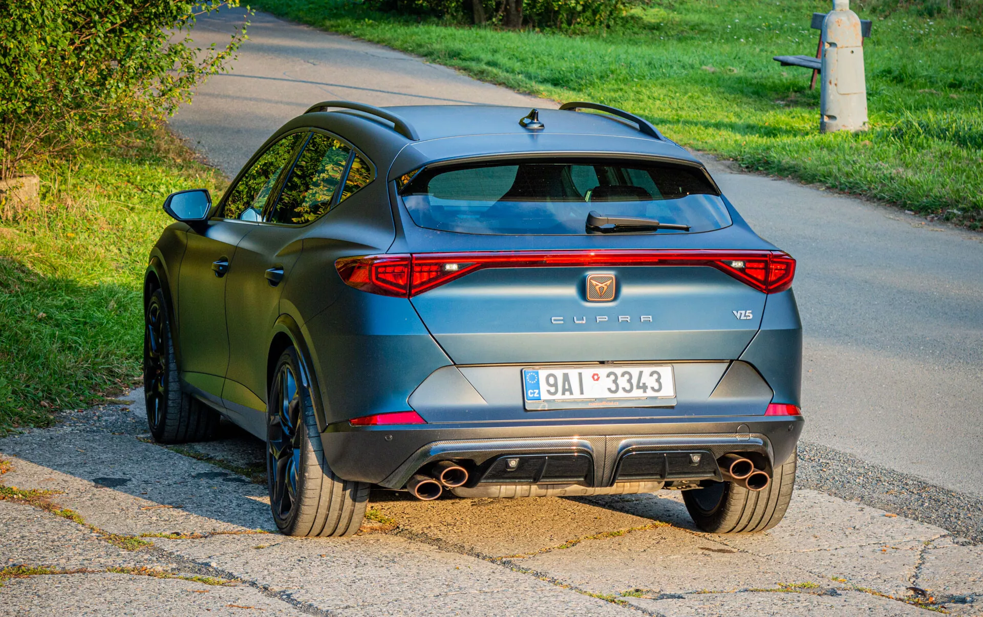 Zadný pohľad na SUV Cupra Formentor VZ5 z roku 2020 s LED zadnými svetlami, štvorcovým výfukovým systémom, športovým zadným difúzorom a nárazníkom, kolesami s viacerými paprskami a matným antracitovým povrchom, fotografovaný vo vonkajšom predmestskom prostredí počas dňa