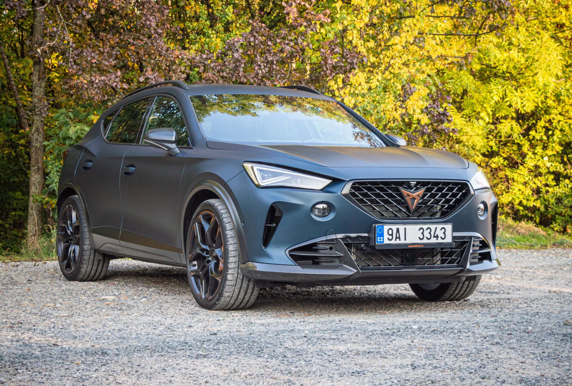 Cupra Formentor 2020 zaparkované na povrchu z štrku s jesenným lístím na pozadí, predvádzajúce jeho matne šedý exteriér, charakteristickú mriežku, LED svetlomety a športové čierne lemy