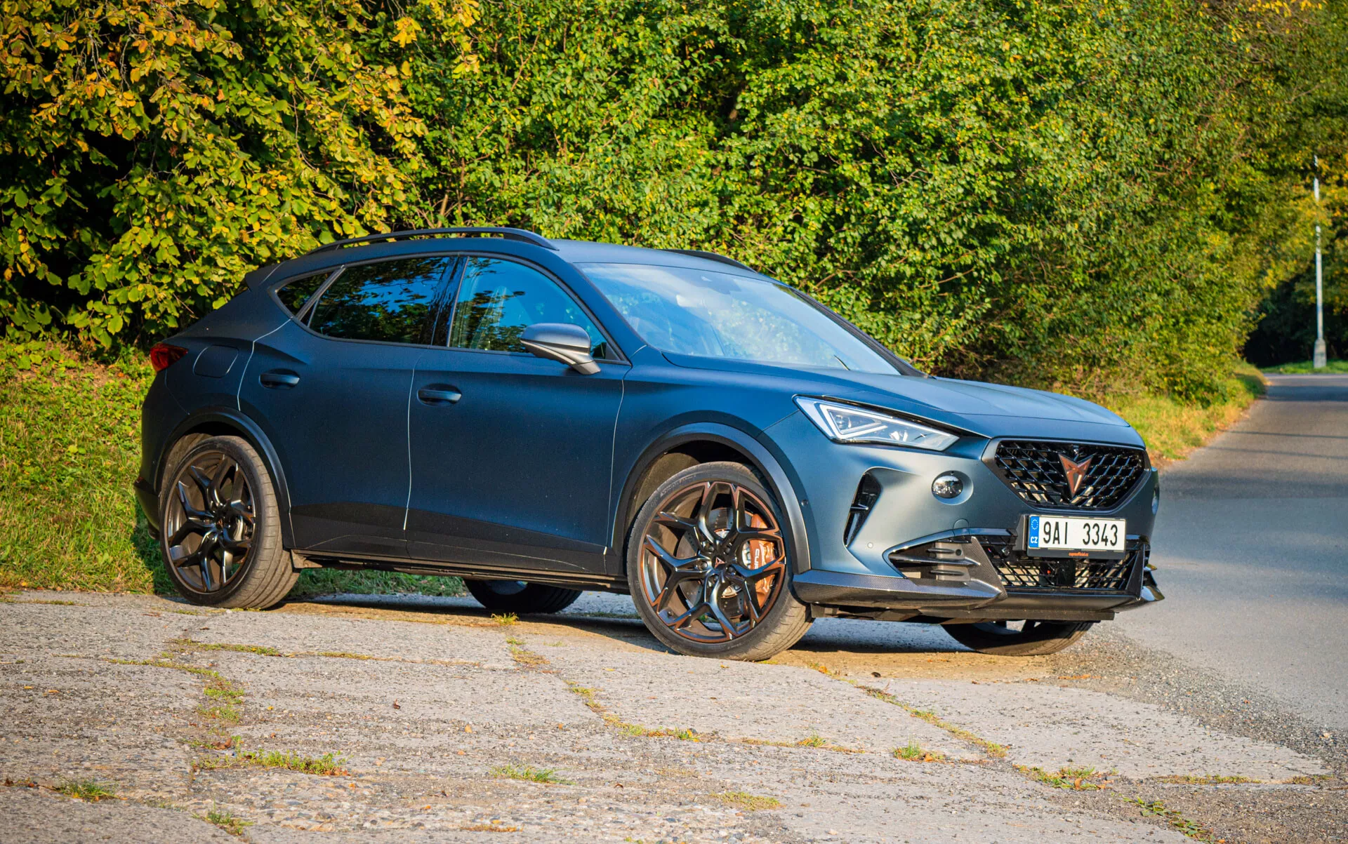 Crossover SUV Cupra Formentor 2020 v tmavo modrej farbe s elegantným dizajnom, LED svetlometmi a päťlúčovými zliatinovými kolesami, fotografovaný z trojštvrtečného predného pohľadu na predmestskú cestu