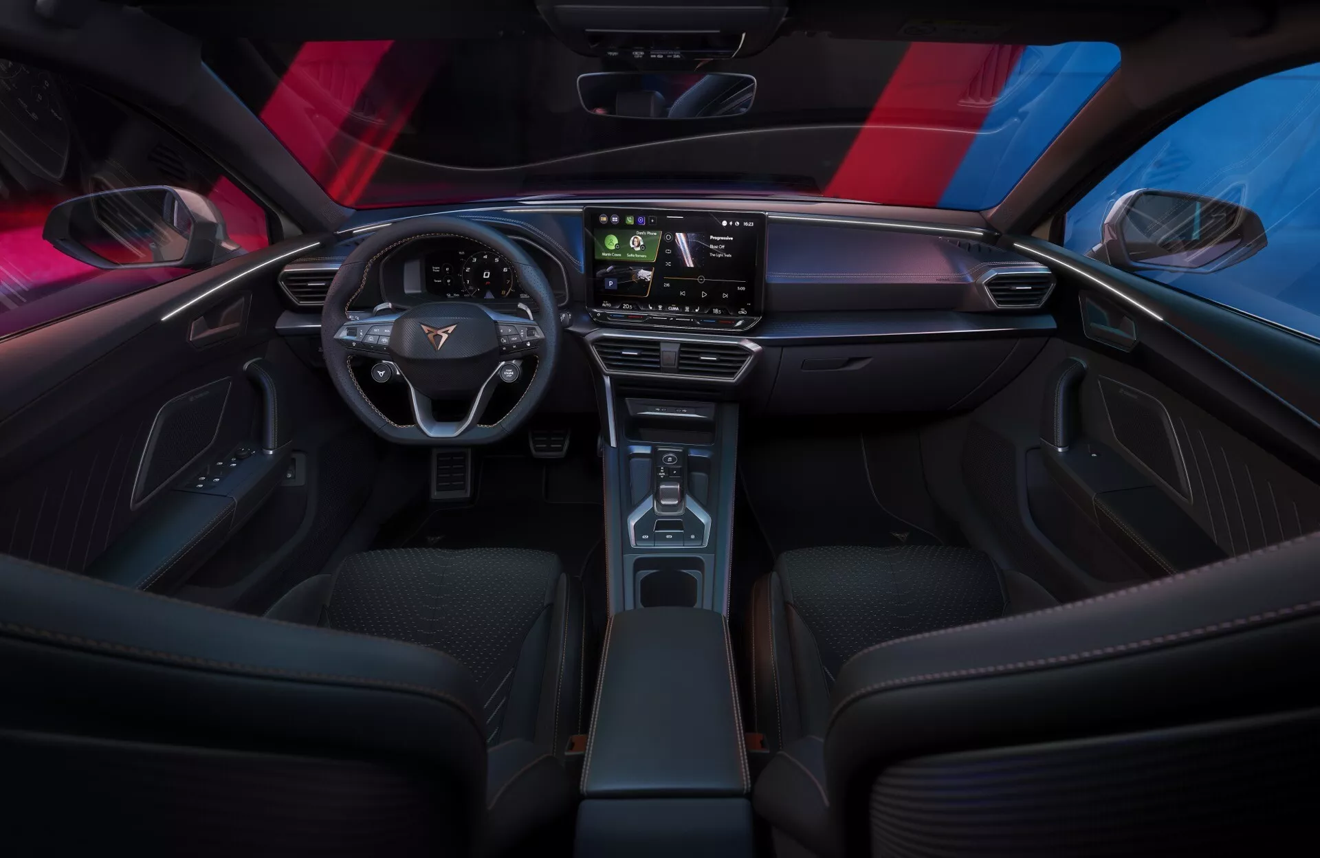 Interiérový záber na Cupra Leon 2024 (facelift 1. generácie) z pohľadu zadného sedadla, ktorý ukazuje elegantnú, minimalistickú palubnú dosku s veľkým dotykovým displejom, moderný dvojramenný volant s ovládacími prvkami vozidla a úzku stredovú konzolu s dreveným dekorom. Športové predné sedadlá, ambientné osvetlenie a panoramatická strecha zdôrazňujú sofistikovanú, technologicky pokročilú atmosféru kabíny.