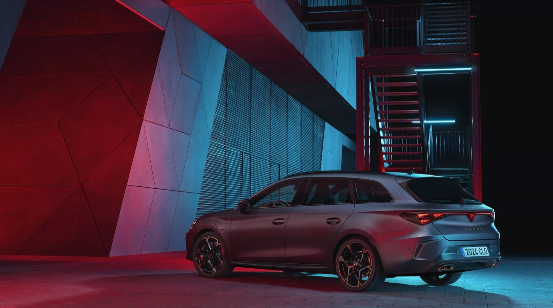 Cupra Leon 2024 prvá generácia facelift fotografovaná z uhla zadnej trištvrtiny zvýrazňujúc pasažérsku stranu. Dramatické nočné osvetlenie zdôrazňuje dizajnové prvky auta, vrátane športových zadných svetiel, zadného nárazníka, agresívneho strešného spojlera a výkonnostne orientovaných ráfikov na pozadí mestského priemyselného prostredia.