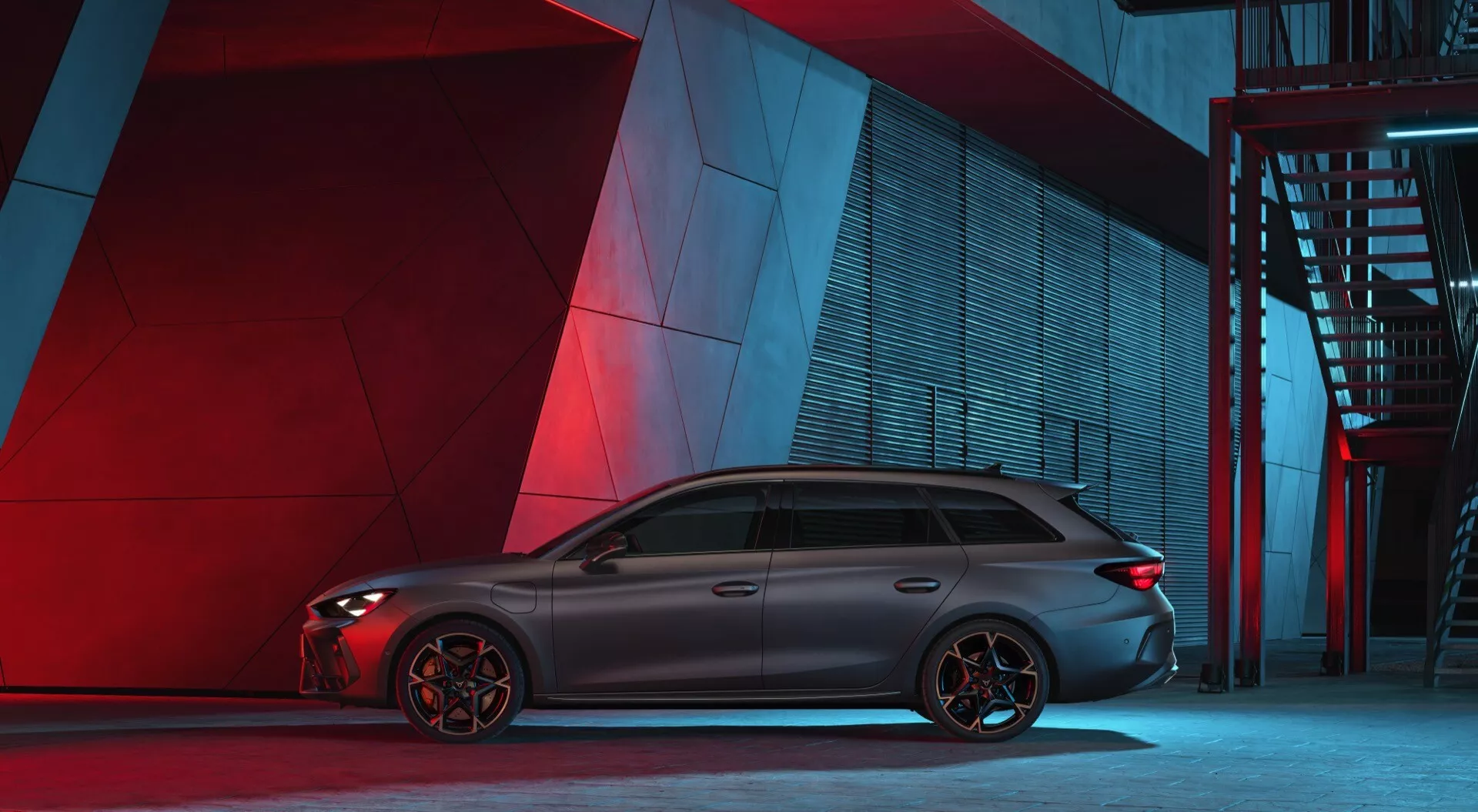Bočný profil športovo vyzerajúceho vozidla Cupra Leon 2024 v mestskom nočnom prostredí s umelým červeným a modrým osvetlením v pozadí. Auto má dlhú, aerodynamickú siluetu, tónované okná s chrómovým lemovaním, strešnú líniu končiacu spoilerom a výrazné viaclúčové zliatinové kolesá. Viditeľné brzdové strmene naznačujú výkonné brzdy. Karoséria má konturované línie a z tohto uhla nie sú viditeľné žiadne ľahko identifikovateľné znaky či technologické prvky.