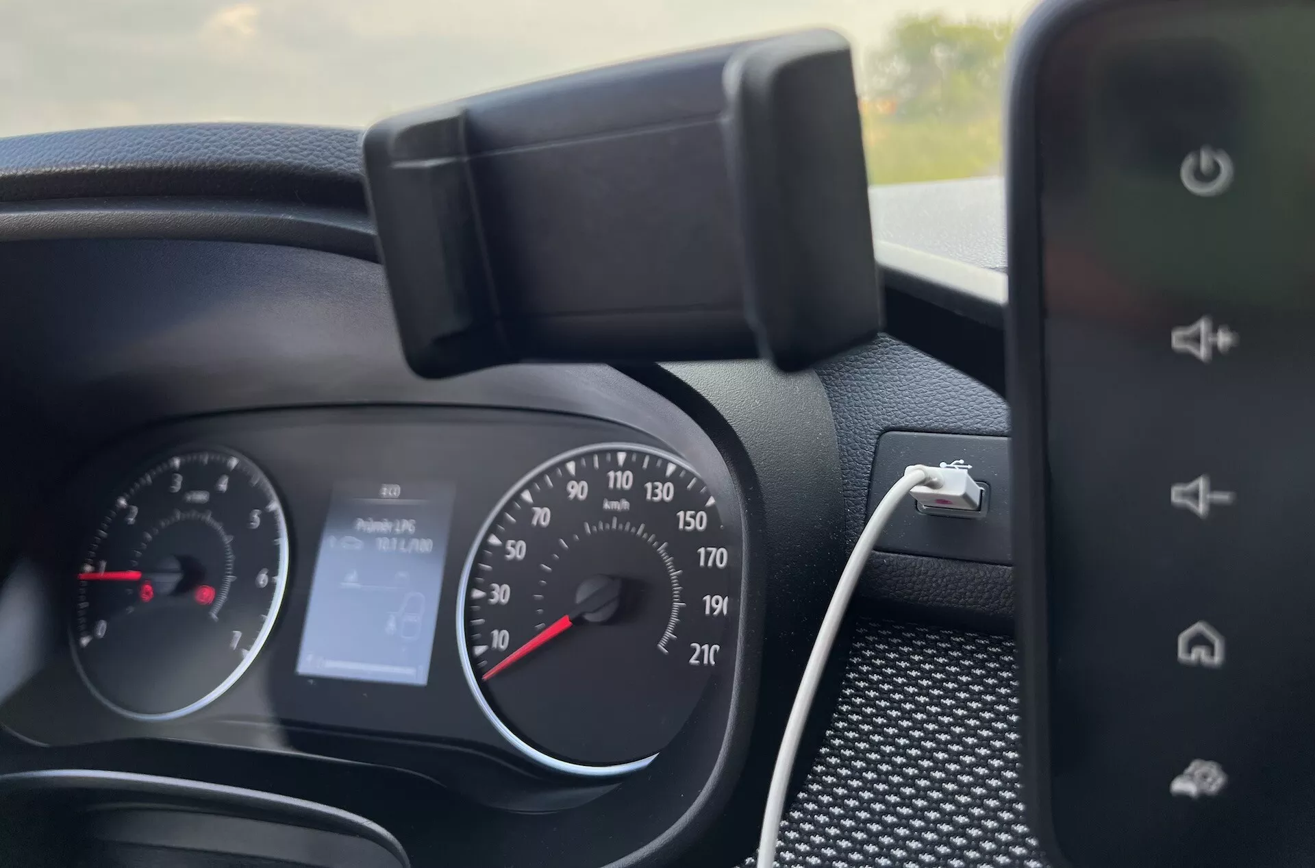 Detailný interiérový pohľad na palubnú dosku Dacia Jogger 2022 ukazujúci prístrojový panel, ovládanie na volante a časť systému infotainment, naznačujúci funkcie ako analógový rýchlostný meter, tachometer, digitálny displej pre 'Žiadne audio' a možnosti nabíjania smartfónu.