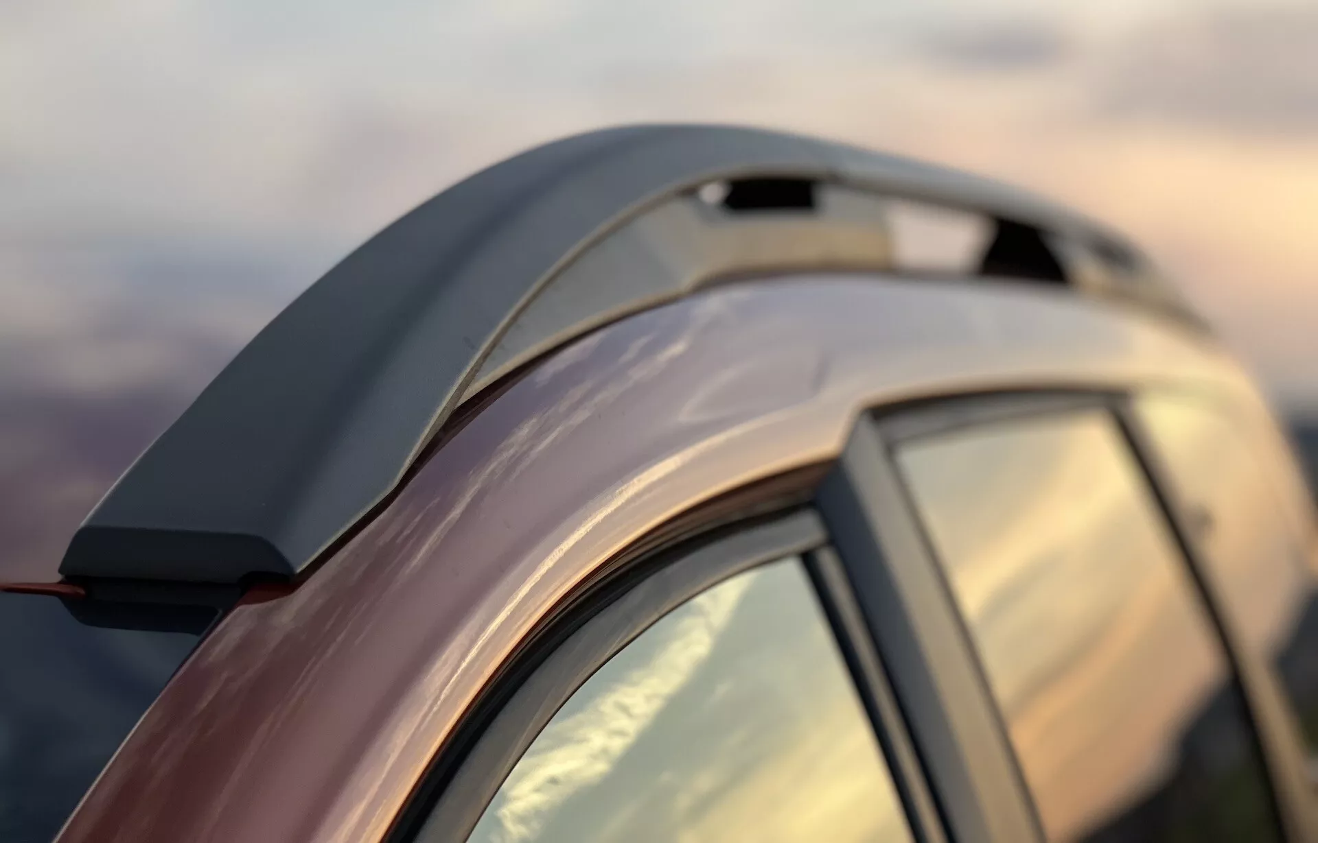 Detailný pohľad na Dacia Jogger 2022 zdôrazňujúci elegantnú líniu strechy, aerodynamické strešné nosiče, integrované zadné krídlo, zatmavené zadné okno s C-stĺpikom, reflexnú metalickú povrchovú úpravu a presnú kvalitu spracovania