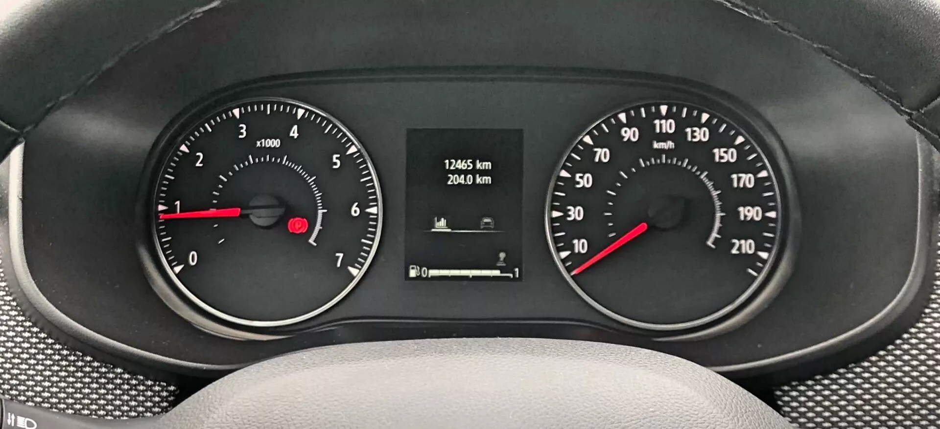 Detailný pohľad na prístrojovú dosku Dacia Sandero-Stepway 2020, zobrazujúci merače s hladkou, textúrovanou palubnou doskou. Analógový otáčkomer vľavo, zobrazujúci rýchlosť motora v otáčkach za minútu (RPM), a rýchlomer vpravo, ukazujúci rýchlosť vozidla v km/h, oba s čiernym pozadím, bielymi číslami a červenými ukazovateľmi. Digitálny displej v strede ukazuje stav tachometra 17465 km a cestovný tachometer 2940 km.