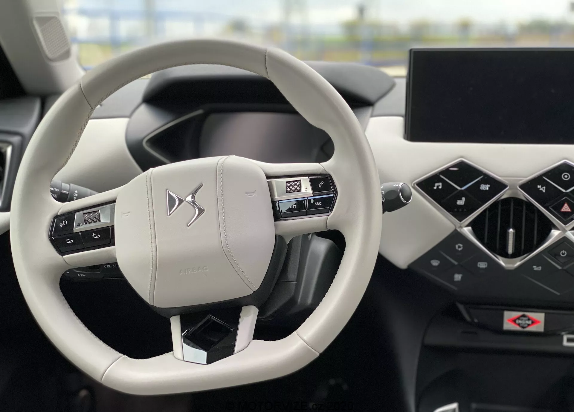 Pohľad na interiér vozidla DS Automobiles DS-3 Crossback E-Tense 2019 so zameraním na volant a prístrojovú dosku z pohľadu vodiča. Dvojramenný volant, potiahnutý kožou so šitím, obsahuje ovládacie prvky pre audio, telefón a nastavenia vozidla. Prístrojová doska zahŕňa digitálny prístrojový panel a veľký infotainment displej orientovaný horizontálne. Minimalistický, moderný dizajn a prémiové materiály zdôrazňujú luxusný zážitok z vozidla.