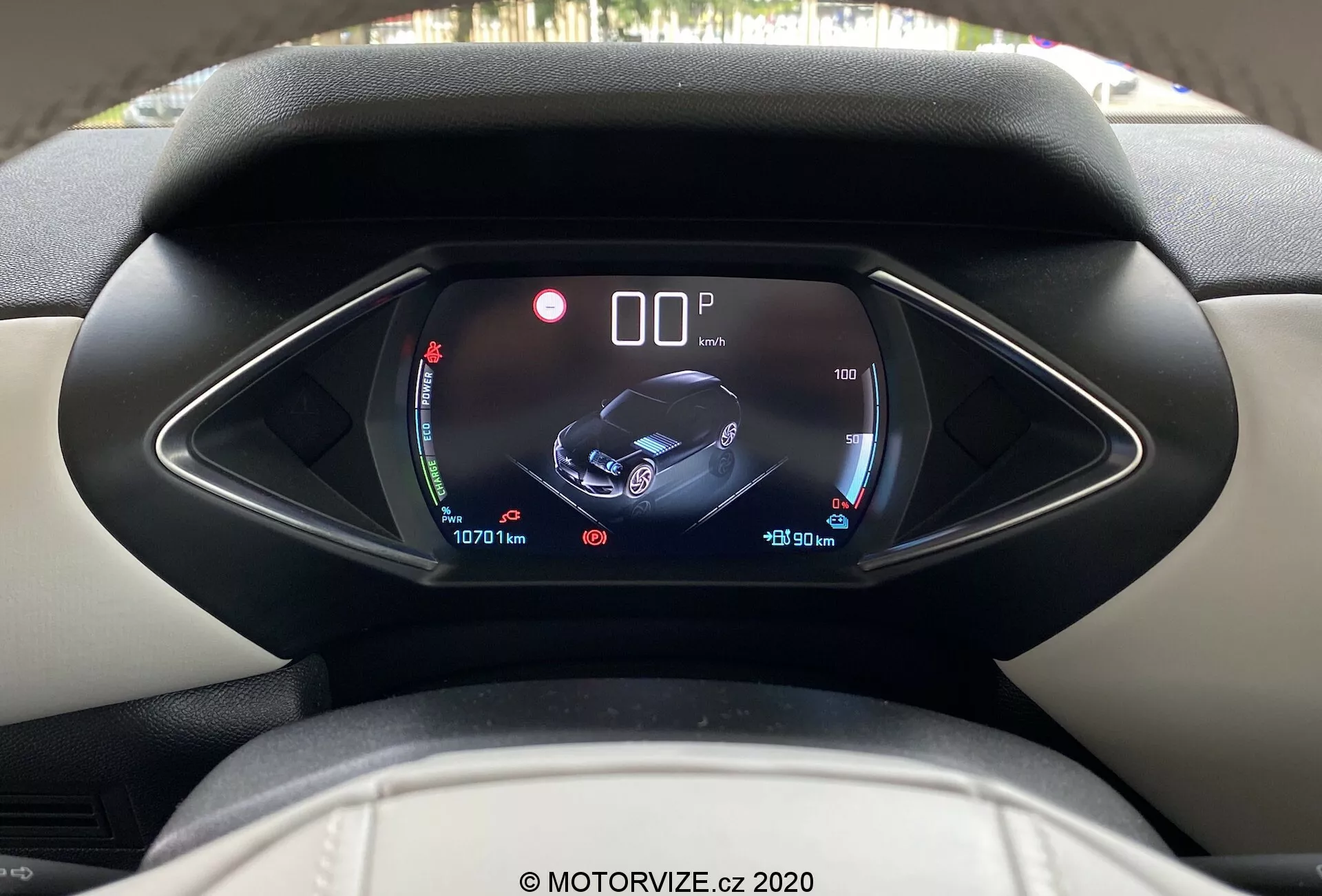Pohľad na interiér auta DS Automobiles DS-3 Crossback E-Tense z roku 2019 z pohľadu vodiča, s dôrazom na digitálny prístrojový panel s unikátnou asymetrickou kapličkou. Displej zobrazuje indikátory nabitia batérie a teploty, centrálnu grafiku auta s ikonami bezpečnostných funkcií a asistencie a informácie o najazdených kilometroch a stave tachometra, čo naznačuje modernú a technologicky vyspelú výbavu interiéru. Čistý a ostrý obraz s vodoznakom MOTORVIZE.cz 2020.