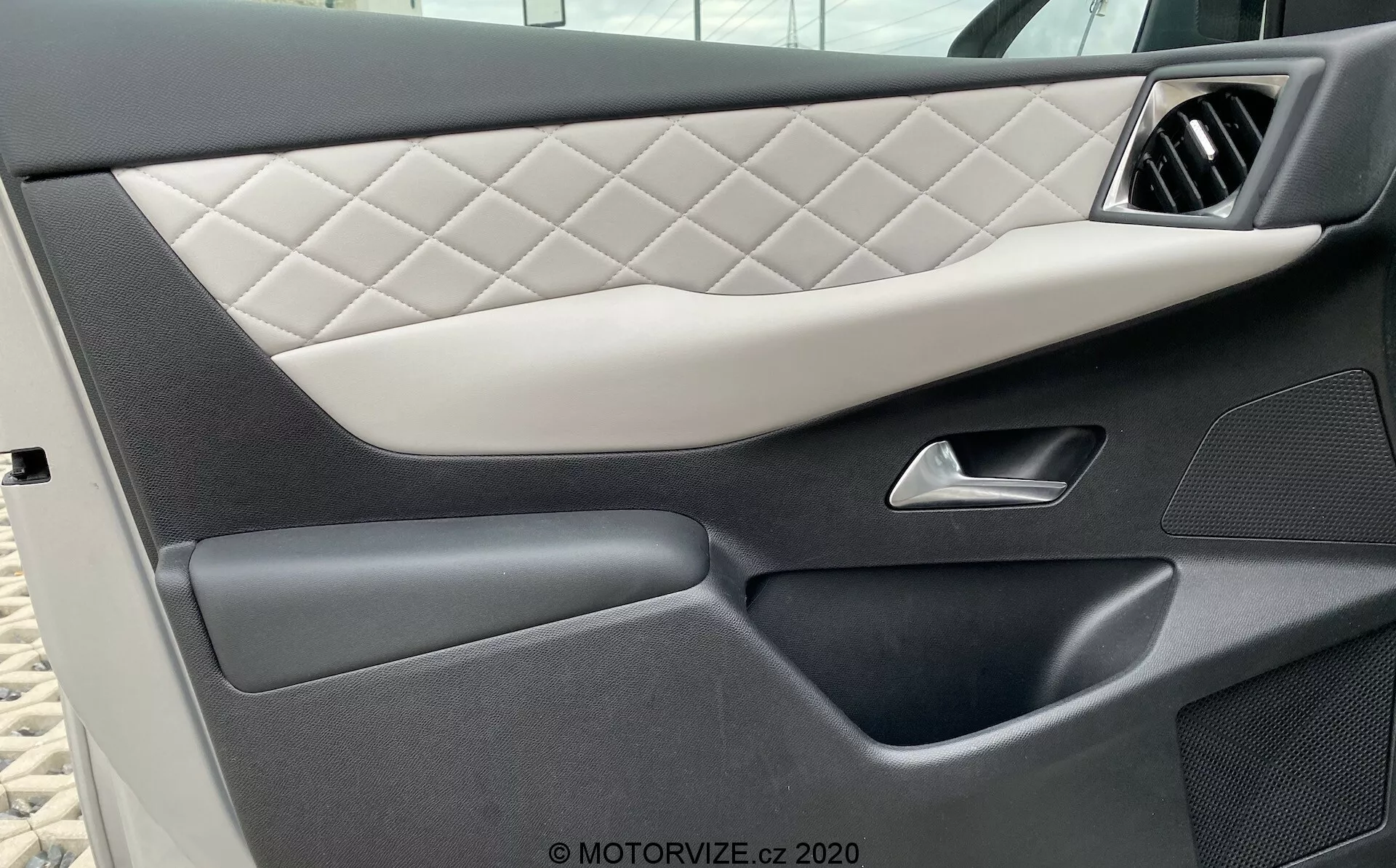 Detailný pohľad na vnútorný dverový panel vozidla DS Automobiles DS-3 2019 (DS-3-Crossback-E-Tense), zobrazujúci prešívané čalúnenie so vzorom diamantu, elegantnú striebornú rukoväť, tmavé vysoko kvalitné plastové sekcie s rôznymi textúrami a bezšvové spodné vrecko na uloženie, zdôrazňujúce luxusný a detailný dizajn vozidla.