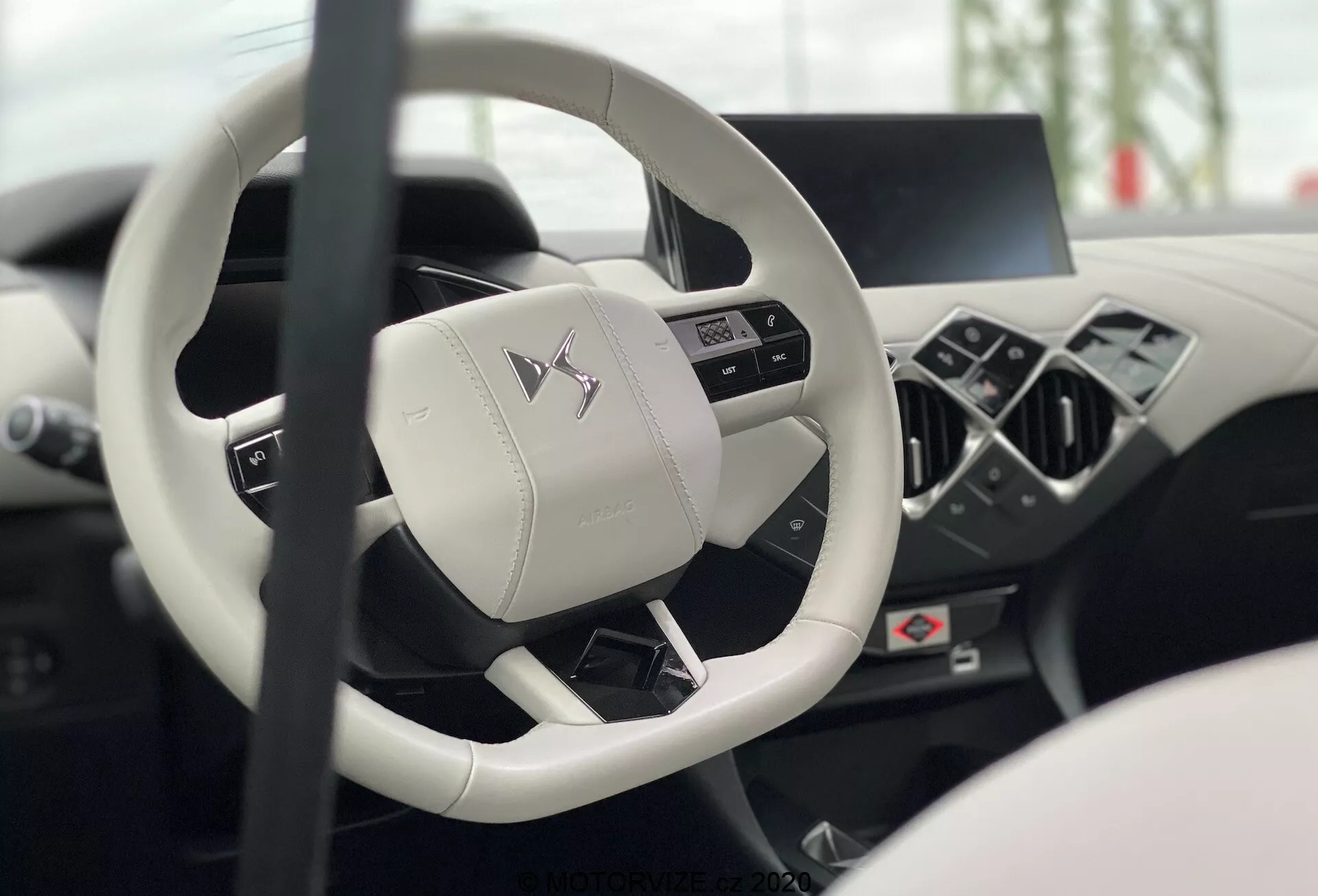 Interiér DS Automobiles DS-3 2019 (DS-3-Crossback-E-Tense) z pohľadu vodiča zameraný na moderný volant s plochým dnom a tromi ramenami s multifunkčnými tlačidlami a rozmazanou digitálnou prístrojovou doskou a stredovou konzolou, ukazujúcimi luxus a pokročilú technológiu