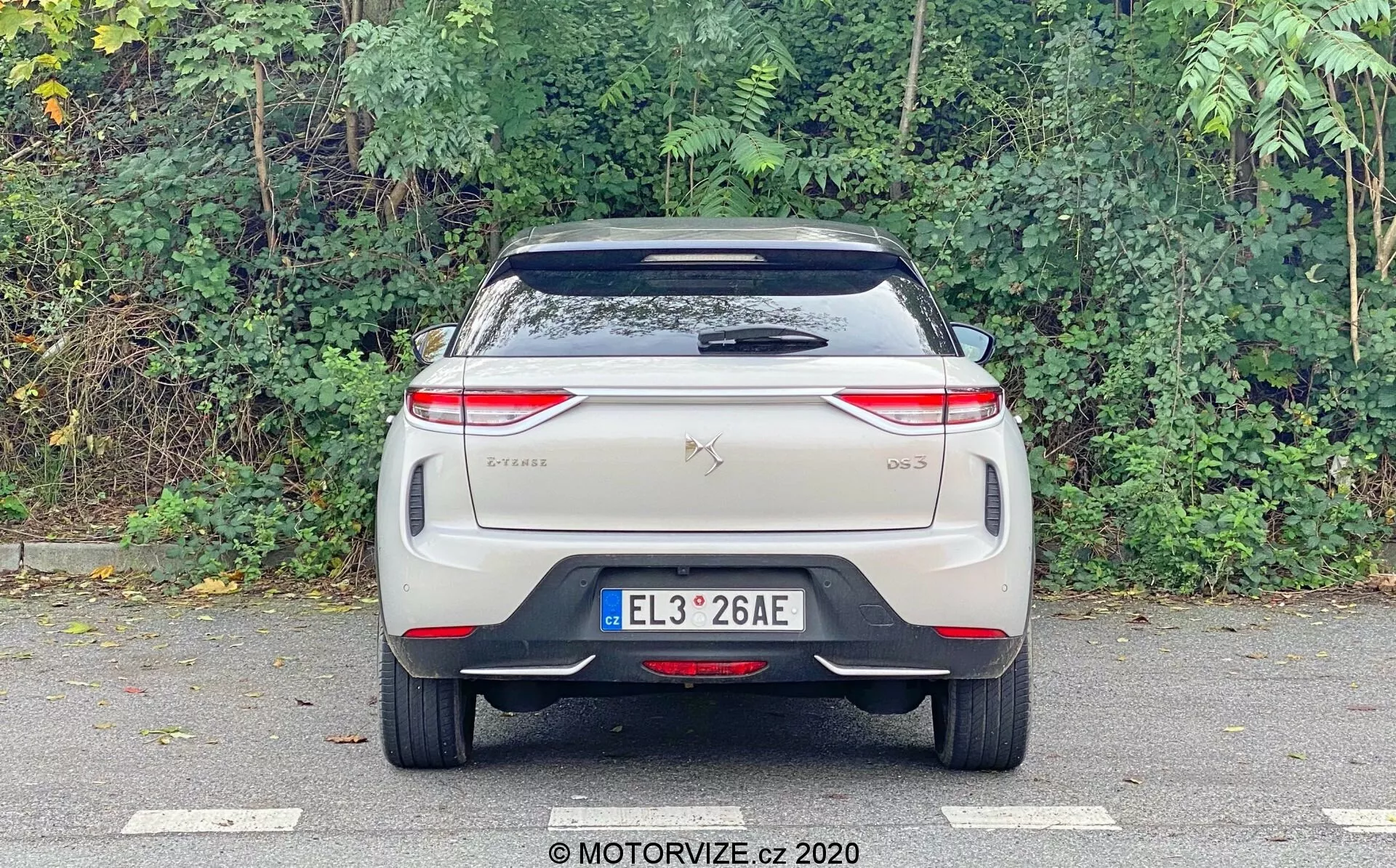 Obrázok zobrazuje zadný pohľad na vozidlo DS Automobiles DS 3 Crossback E-Tense z roku 2019, fotografovaný na úrovni očí so zameraním na zadnú stranu. Viditeľné prvky zahŕňajú centrálne umiestnenú registračnú značku, odznaky značky a modelu na kufri, moderné horizontálne orientované zadné svetlá s prepracovanými LED vzormi, zadné čelné sklo s stieračom, strešný spojler a nárazník s reflexným pruhom. Nevidno tradičné koncovky výfuku, čo naznačuje, že ide o elektrické vozidlo. Dizajn je čistý, pravdepodobne obsahuje pokročilé technologické črty typické pre elektrické alebo hybridné vozidlá.