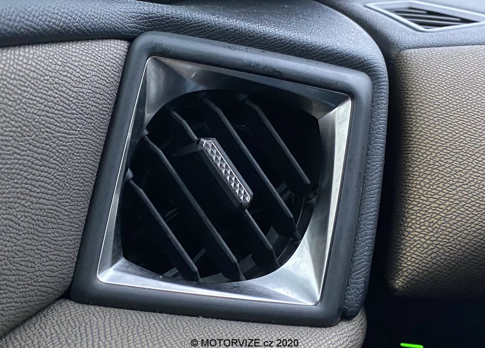 Detailný pohľad na ventiláciu vo vnútri vozidla DS Automobiles DS-3 Crossback z roku 2019, zobrazujúcu nastaviteľné horizontálne lamely v diamantovom otvore obklopenom plastovým povrchom prístrojovej dosky so štvorcovým rámčekom pre zvýšenie dizajnu.