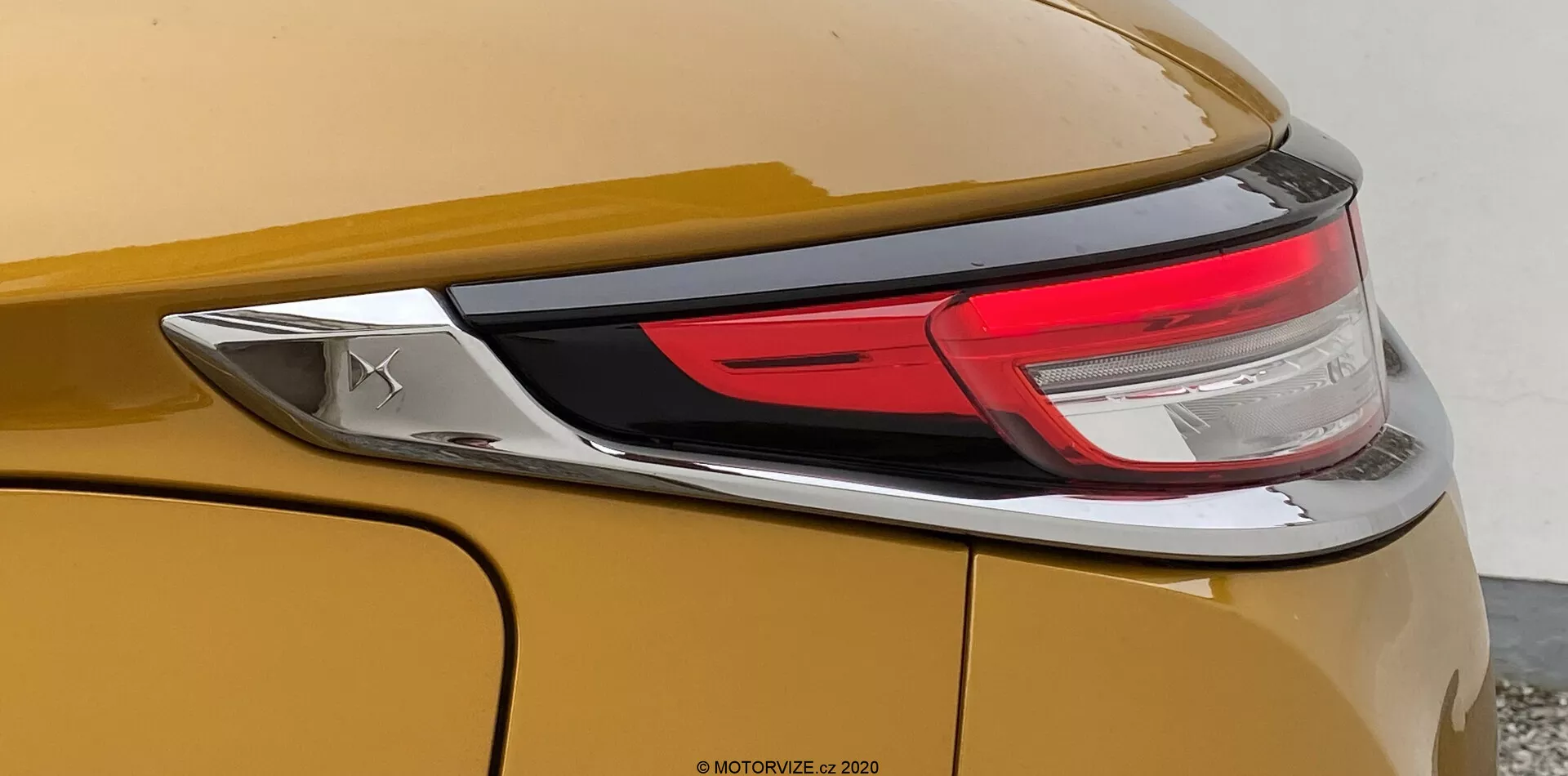 Detailný pohľad na zadnú časť vozidla DS Automobiles DS-3 2019 (DS-3 Crossback). Obrázok sa zameriava na pravú stranu vozidla, ukazuje kovovú zlatú alebo bronzovú karosériu, časť LED zadného svetla a hladký, zakrivený zadný panel s výraznou líniou. Je vidno aj chrómovaný emblém, ale značka nie je rozpoznateľná.