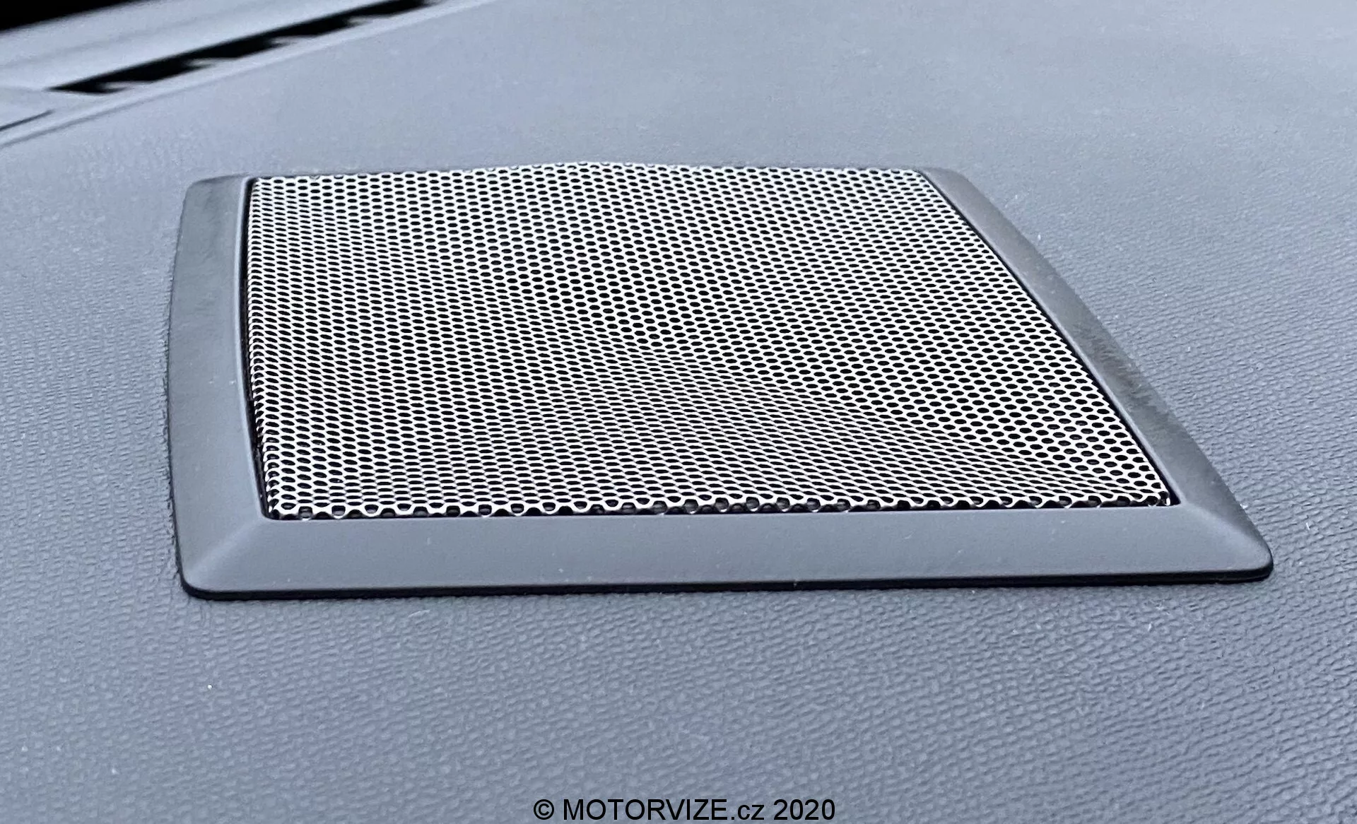 Detailný pohľad na mriežku reproduktora na palubnej doske vozidla DS Automobiles DS-3 Crossback 2019. Trapezová mriežka s hustou sieťovinou na ochranu reproduktora a elegantným, neodrážavým okrajom, ktorý ladí s palubnou doskou.