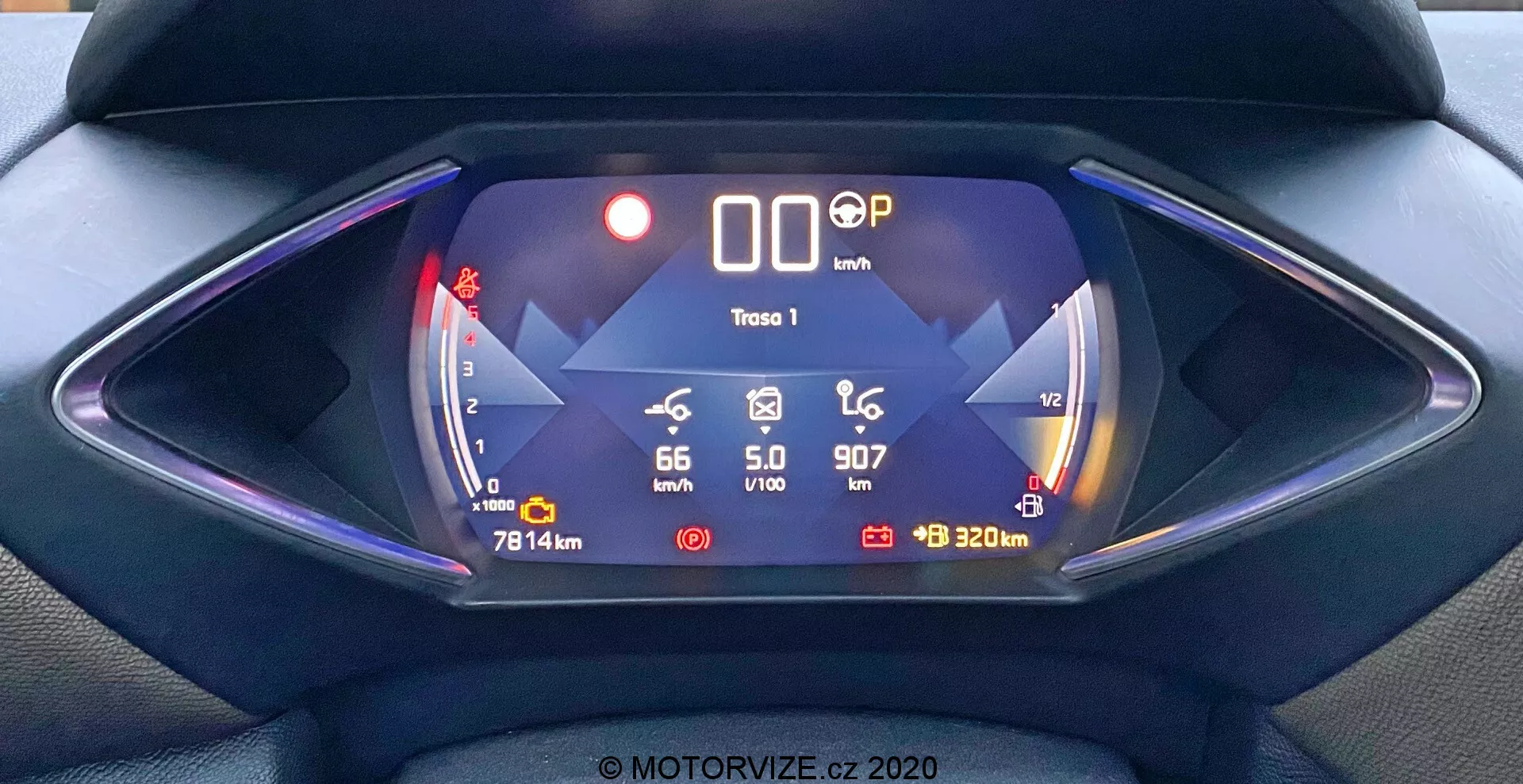 Digitálny prístrojový panel vozidla DS Automobiles DS-3 2019 (DS-3 Crossback) z pohľadu vodiča. Symetrická kompozícia sa zameriava na futuristický šesťuholníkový prístrojový panel s modro laděným digitálnym displejom. Funkcie zahŕňajú ukazovateľ dojazdu batérie zobrazujúci '66 km' vľavo, rýchlosť '0 km/h' v strede, polohu radenia 'P', ikonu klzkej cesty a ukazovateľ '320 m' vpravo. Ďalšie údaje zahŕňajú vonkajšiu teplotu '5,0°C', aktuálny čas '9:07' a nájazd vozidla '7814 km'. Tento obraz zdôrazňuje vlastnosti elektrického alebo hybridného vozidla s pokročilou technológiou a digitálnymi infografikami.