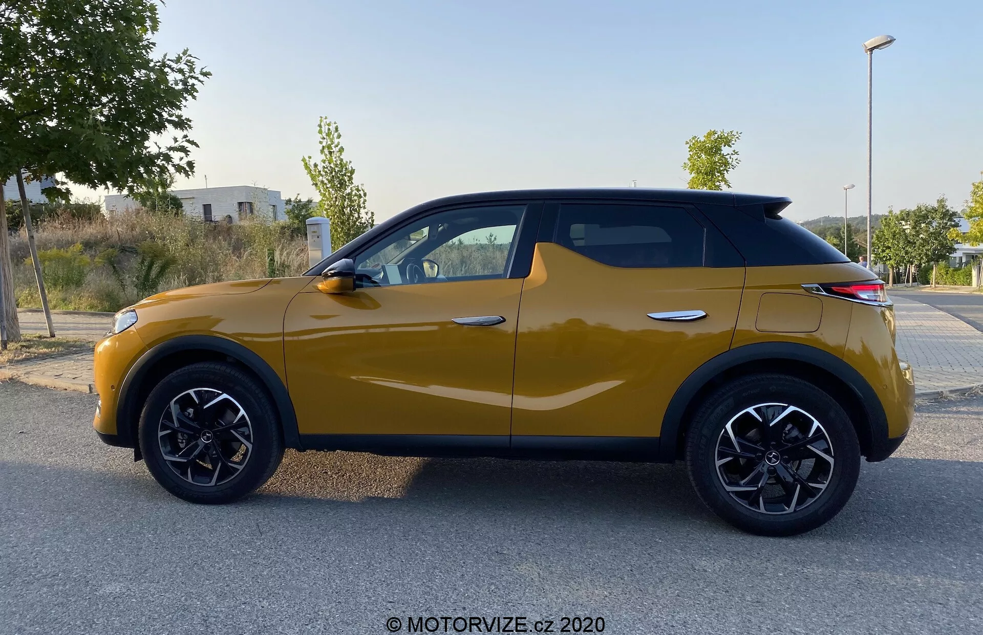 Bočný profil vozidla DS Automobiles DS 3 Crossback z roku 2019 v horčicovo žltej farbe. Moderné kompaktné SUV s výraznými čiernymi oblúkmi kolies, čiernymi viacramennými zliatinovými kolesami a dynamickou karosériovou linkou od predného kolesa po zadné svetlá. Integrované smerovky v bočných zrkadlách a čierne kontúry okien zvýrazňujú súdržný dizajn, zatiaľ čo strecha v štýle kupé dodáva súčasný vzhľad. Fotografia bola zhotovená pri rozptýlenom svetle, bez tieňov alebo odleskov, s dôrazom na dizajnové prvky vozidla.