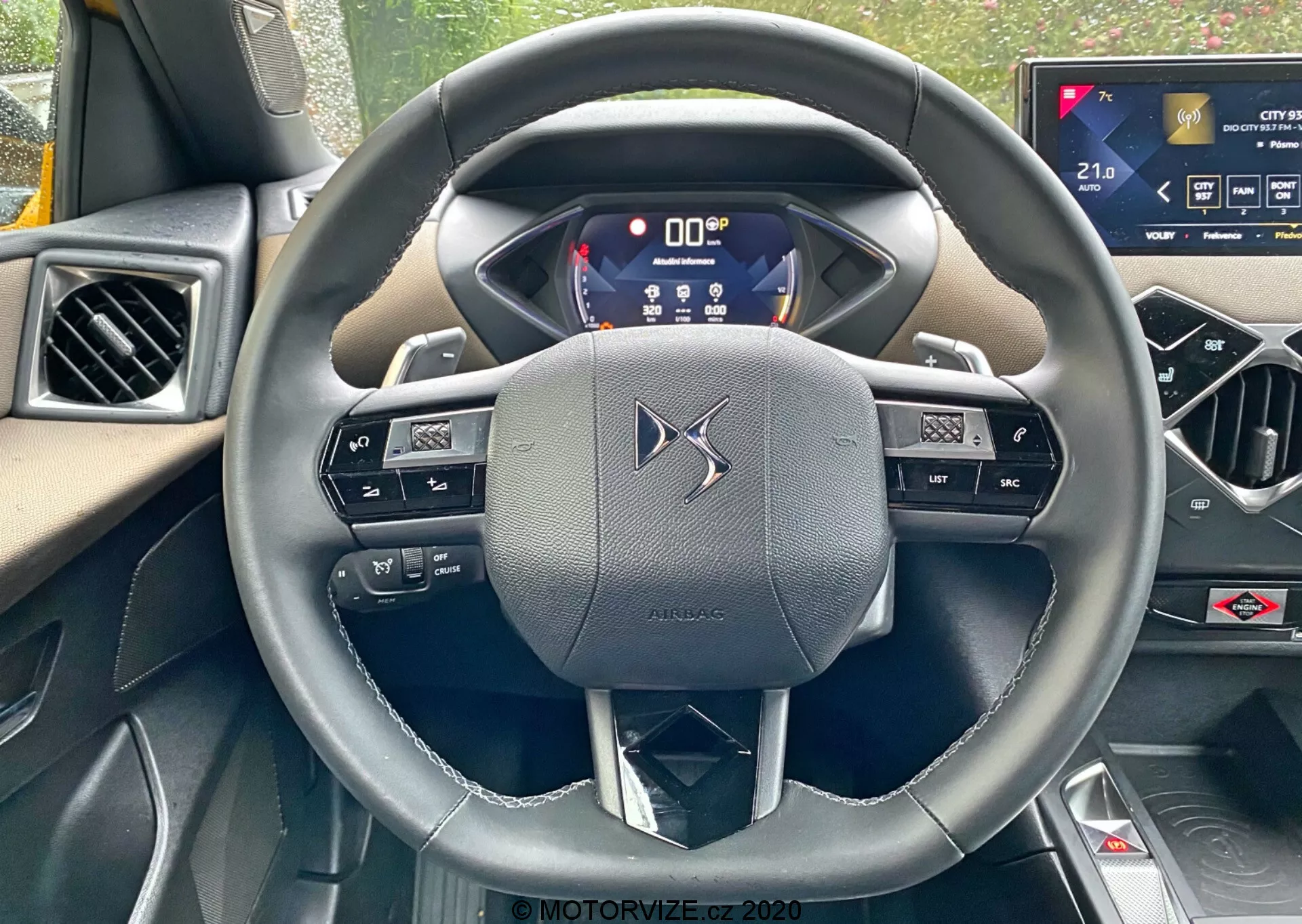 Pohľad z prvej osoby zo sedadla vodiča v DS-Automobiles DS-3 2019 (DS-3 Crossback), zameraný na trojramenný kožený volant s integrovanými ovládačmi a páčkovými spínačmi. Digitálny prístrojový panel zobrazuje kľúčové informácie, čo zdôrazňuje pokročilú technológiu vozidla. Dotykový infotainment systém na stredovej konzole naznačuje vysokú úroveň komfortných funkcií vozidla.