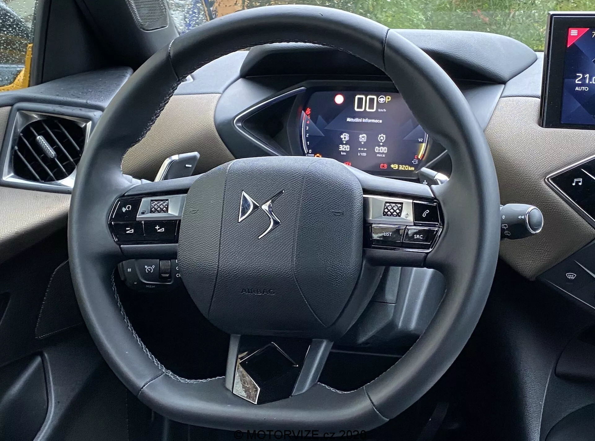Pohľad na interiér vozidla DS Automobiles DS-3 2019 (DS-3 Crossback) z perspektívy vodičovho sedadla, s volantom obsahujúcim tlačidlá na ovládanie multimédií, hlasové povely a tempomat, aktívnym digitálnym prístrojovým panelom zobrazujúcim rôzne informácie o vozidle a časťou infotainmentového systému s možným pripojením pre smartfóny a navigačnými schopnosťami. Interiér obsahuje kombináciu mäkkých plastov a chrómových akcentov, čo ukazuje modernú technológiu a estetický pôvab.