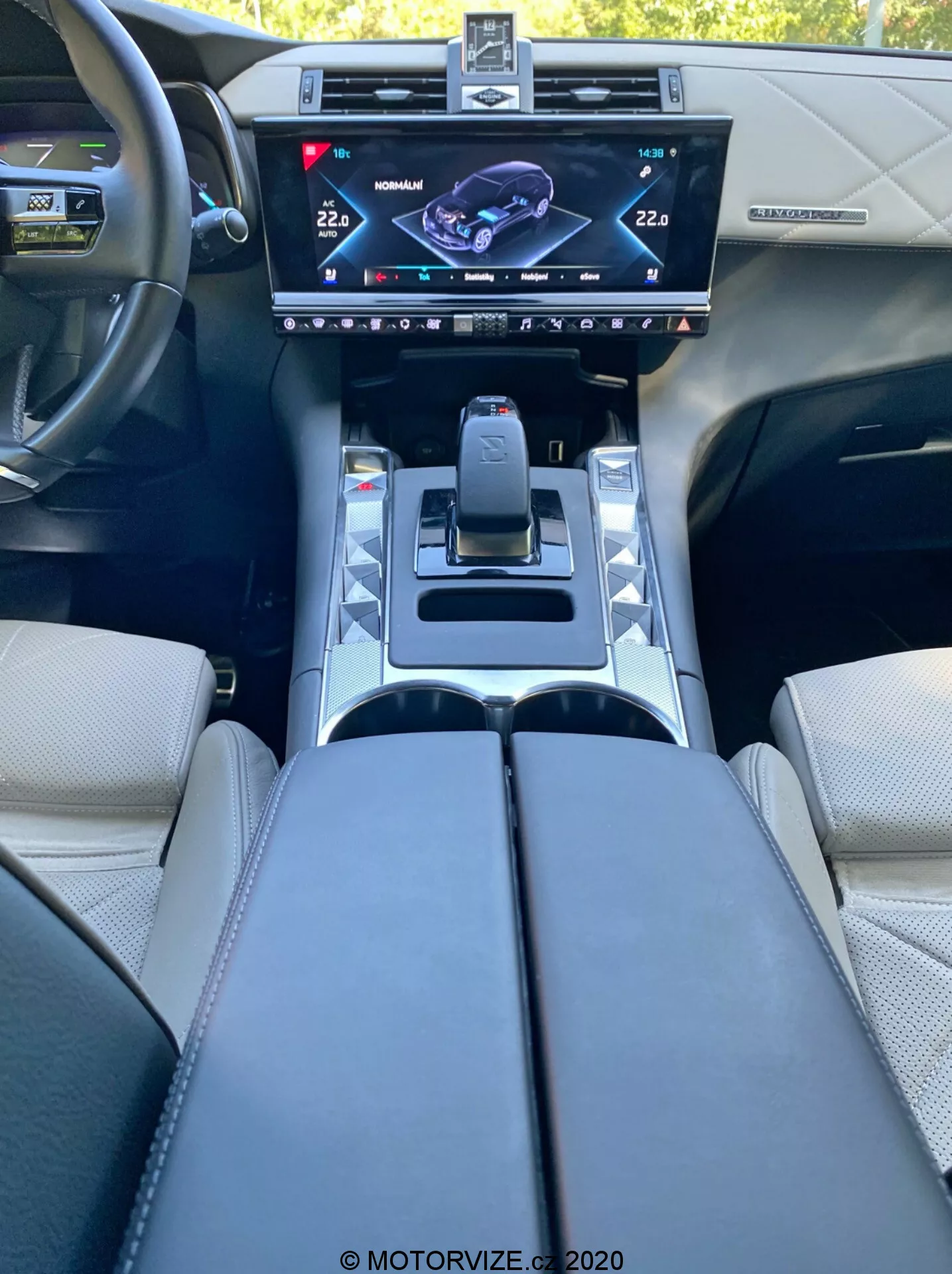 Pohľad do interiéru vozidla DS Automobiles DS 7 Crossback z roku 2018 z pozície vodiča, zobrazujúci centrálnu konzolu s vysokokvalitným dotykovým displejom infotainmentu, moderným voličom prevodov, tlačidlami jazdných režimov, držiakmi na nápoje, čalúnenými opierkami rúk a volant s ovládacími tlačidlami, odrážajúce špičkový automobilový dizajn a technológie.