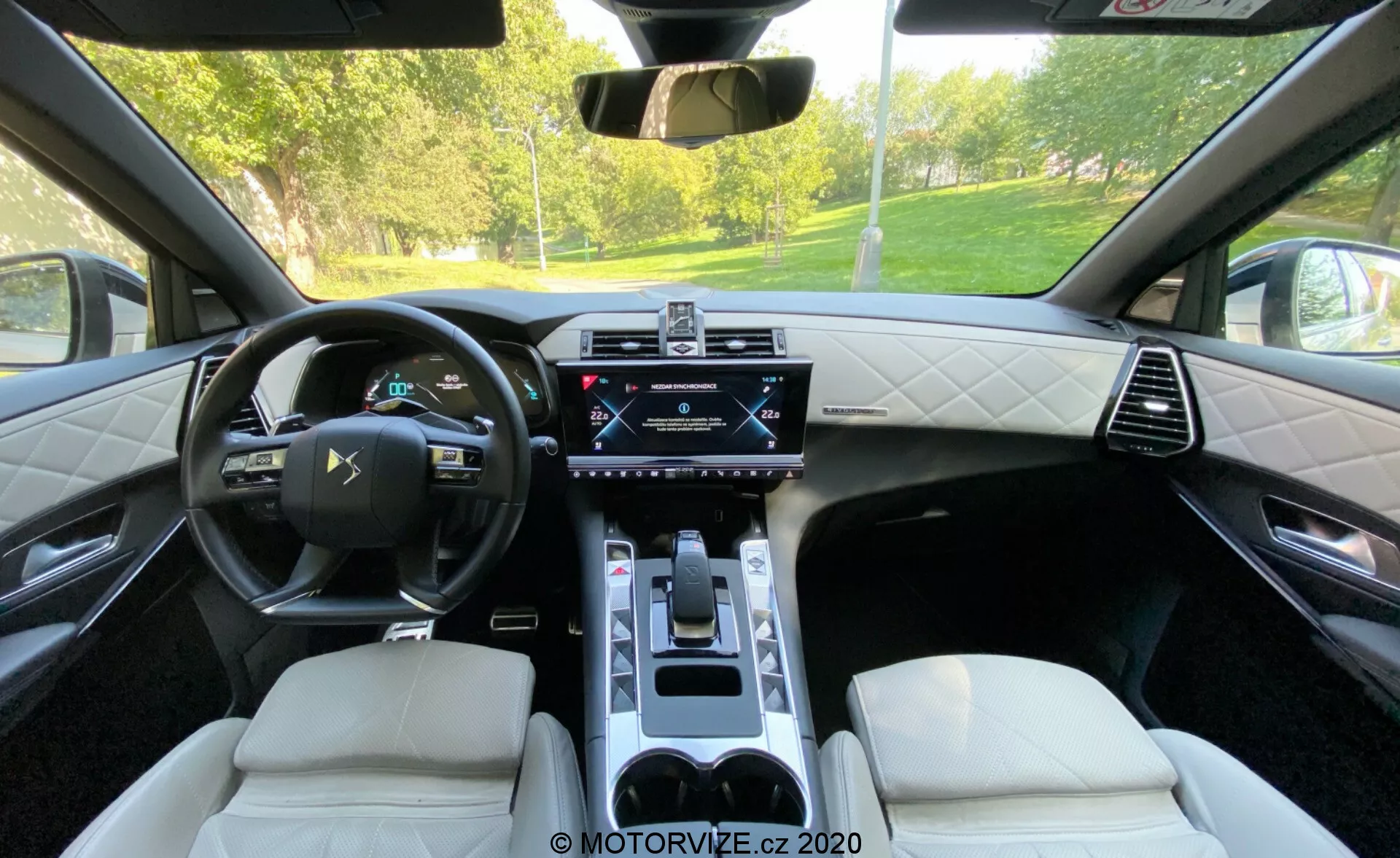 Záber na interiér DS Automobiles DS 7 Crossback 2018 z pohľadu zadného sedadla, zvýrazňujúci kožený multifunkčný volant, digitálny pristrojový klastr, centrálny dotykový displej infotainmentu, panel ovládania klimatizácie, elektronický volič prevodovky, luxusné kožené sedadlá s diamantovým prešívaním a stredovú konzolu s držiakmi na poháre. Obrázok ukazuje kombináciu najmodernejšej technológie a sofistikovaného dizajnu.