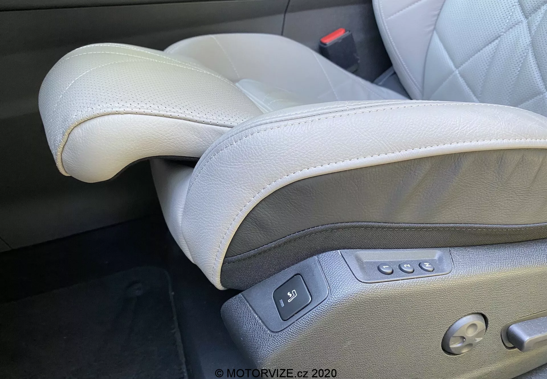 Detailný záber na interiér DS Automobiles DS-7 2018 (DS-7 Crossback), zameraný na luxusné, svetlošedé kožené sedadlo vodiča umiestnené na ľavej strane v konfigurácii s ľavostranným riadením. Viditeľné prvky zahŕňajú vysoko kvalitnú kožu so šitím, nastaviteľnú opierku hlavy, elektrické ovládanie sedadla s viacerými tlačidlami pre posuv, naklápanie, nastavenie výšky a bedernú oporu, ako aj tlačidlo nastavenia pamäte a viditeľnú pracku bezpečnostného pásu, čo zdôrazňuje prémiový a ergonomický dizajn.