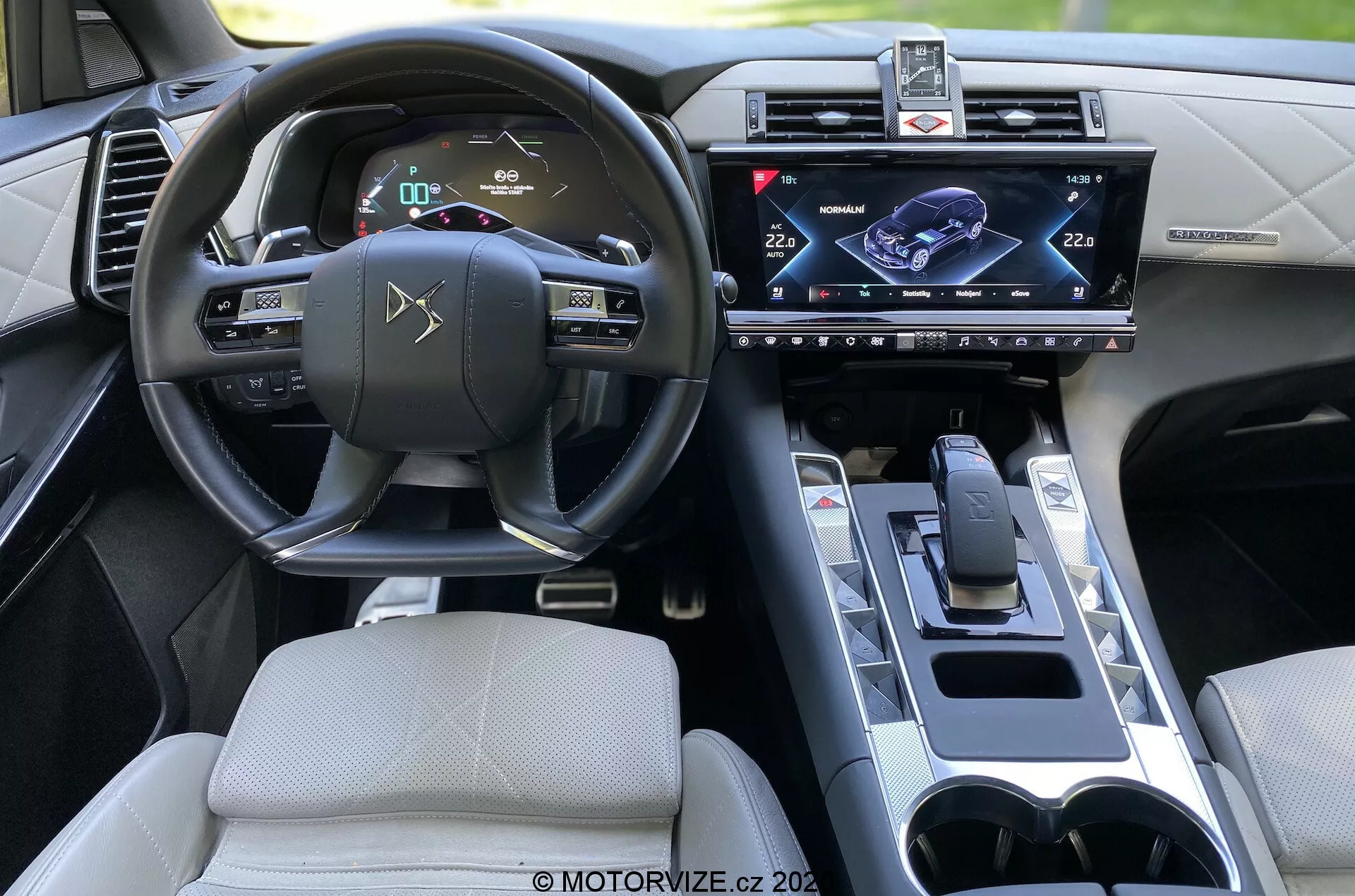 Interiér DS Automobiles DS 7 Crossback 2018, pohľad zo zadného sedadla zameraný na stranu vodiča. Funkcie zahŕňajú volant s integrovanými ovládacími prvkami, digitálny prístrojový panel, centrálne umiestnený dotykový infotainment systém, modernú radiacu páku, držiaky na poháre a sofistikovaný dizajn interiéru s pokročilými technologickými vybaveniami.