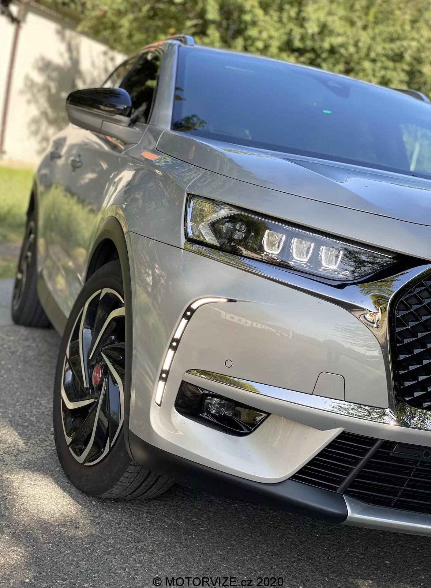 Detailný pohľad spredu na DS Automobiles DS 7 Crossback 2018, ktorý zachytáva ľavú prednú štvrtinu, ukazuje elegantné LED svetlá, výrazná zložitá mriežka, tvarovaná kapota, viacramenné zliatinové kolesá s nízkoprofilovými pneumatikami, metalický lak, bočné zrkadlo v farbe karosérie a dynamické odrazy naznačujúce vonkajšie prostredie.