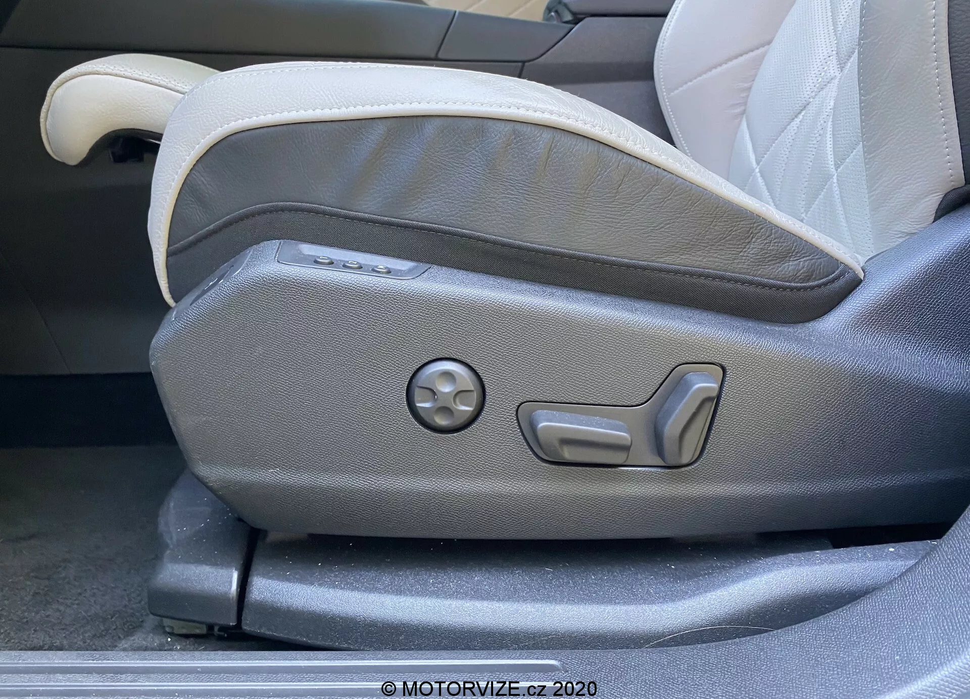 Zblízka ovládací panel na nastavenie predného sedadla vodiča v DS Automobiles DS 7 Crossback z roku 2018. Obrázok zachytáva elektricky ovládané prvky pre nastavenie sedadla, vrátane tlačidiel pre viacúrovňové nastavovanie a kruhového otočného ovládača pre pamäťové nastavenia. Sedadlo má dvojfarebné čalúnenie vo svetlých a tmavých šedých odtieňoch, ktoré zdôrazňujú moderný a ergonomický dizajn charakteristický pre luxusné automobily.