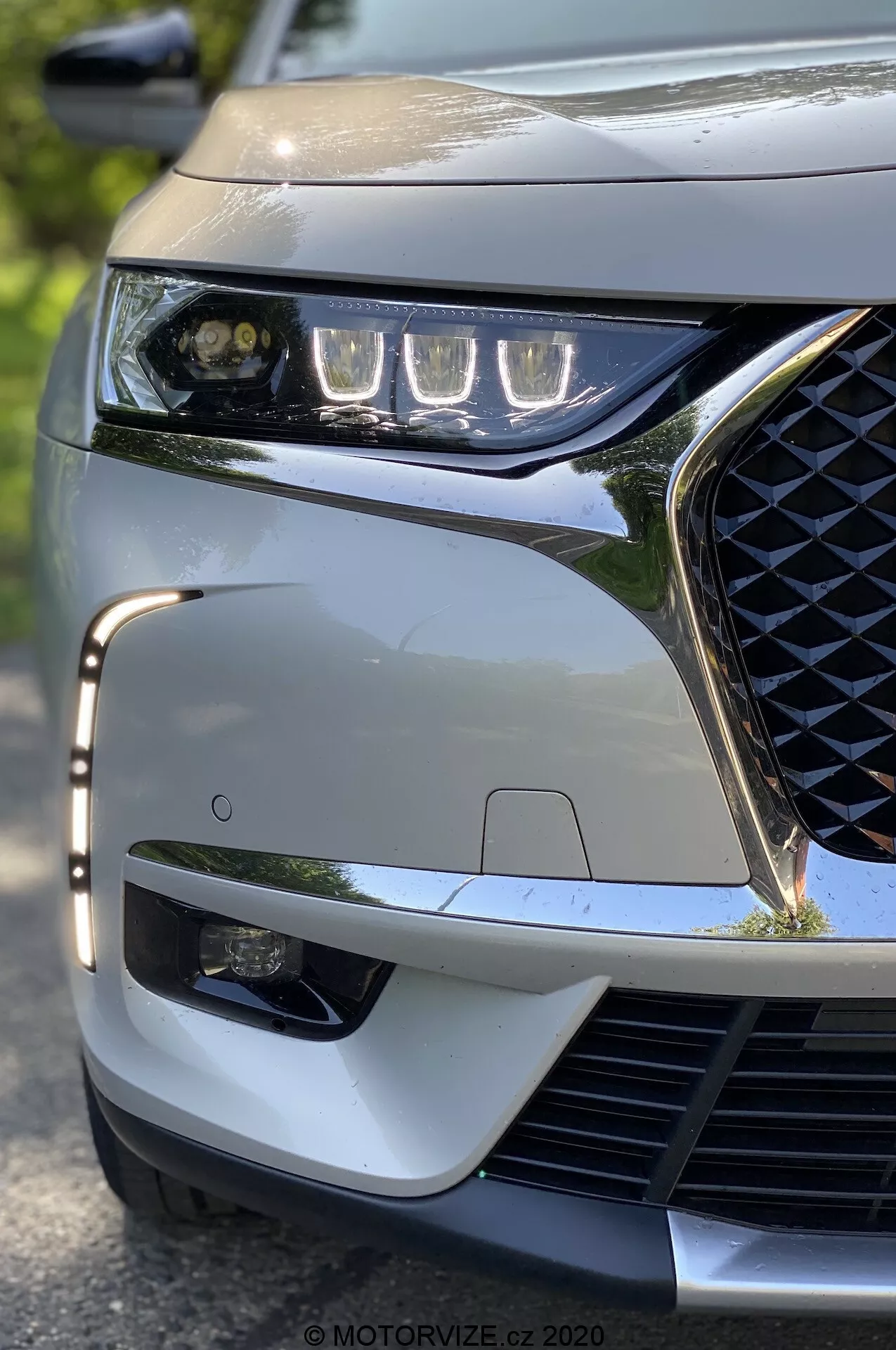 Detailný záber z nízkeho uhla na predný ľavý roh modelu DS Automobiles DS 7 Crossback z roku 2018. Zdôraznené sú elegantné LED svetlomety, geometricky vzorovaná mriežka chladiča, športový predný nárazník a viditeľný senzor ADAS, čo podčiarkuje moderné technologické a estetické črty vozidla.