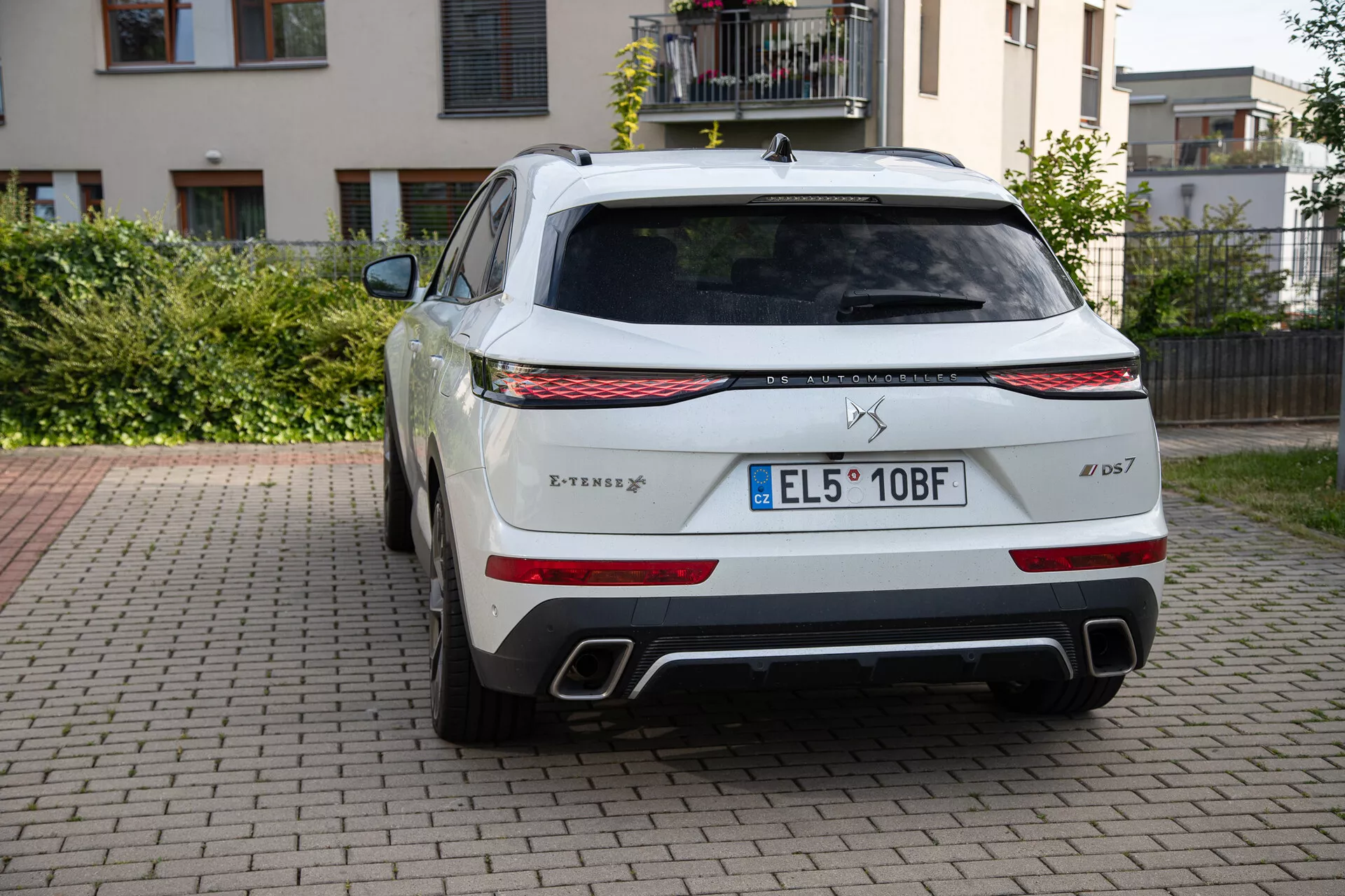 Zadný pohľad na zaparkovaný DS Automobiles DS 7 2022 na dlažbe s rezidenčným pozadím, zobrazujúci logo tridentu, názov modelu Levante, známku úpravy S, LED zadné svetlá, dvojité chrómové výfuky, čierny difúzor, veľké zadné čelné sklo so stieračom, európsku evidenčnú značku, parkovacie senzory, odznak systému pohonu všetkých kolies Q4 a anténu v tvare žraločej plutvy.