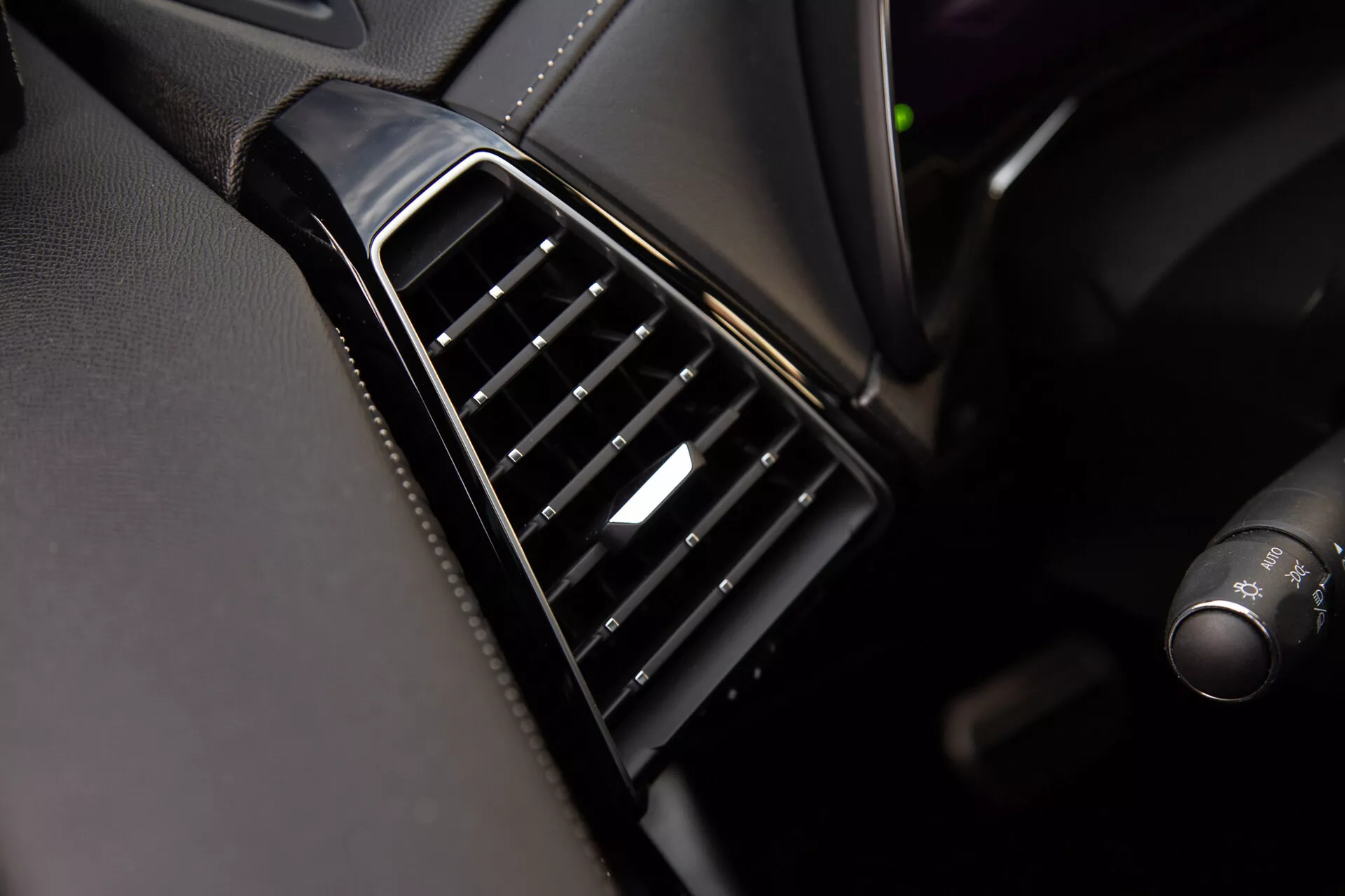 Detailný pohľad na ventilačnú mriežku DS Automobiles DS-7 2022 na prístrojovej doske s vertikálne zarovnanými čiernymi nastaviteľnými lamelami, lesklým lemom a strieborným akcentom na ovládači, predvádzajúci kvalitu a materiály interiéru vozidla