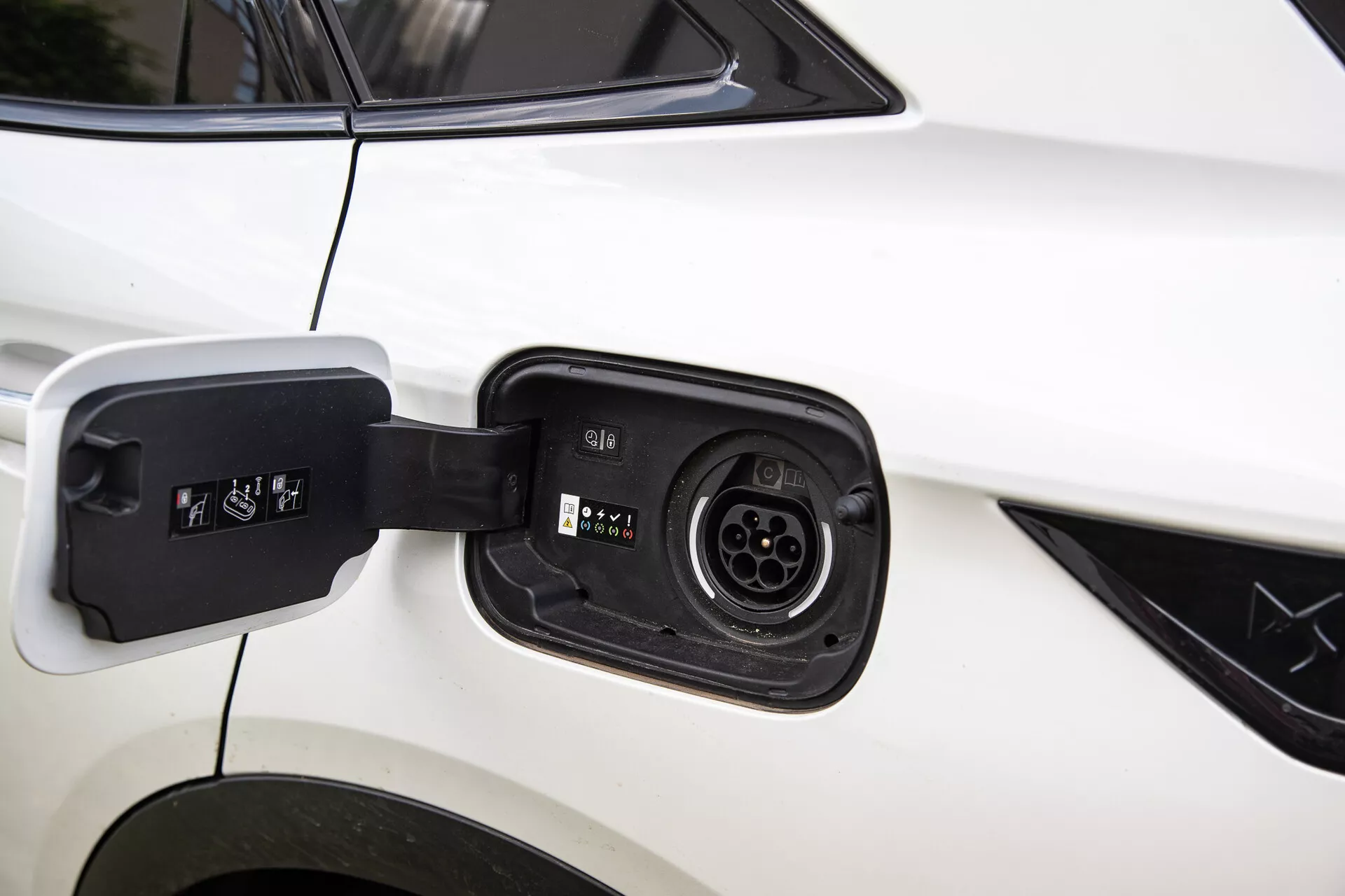 Detailný pohľad na nabíjací port elektrického hybridného vozidla DS Automobiles DS-7 2022, ukazujúci kompatibilitu s viacerými nabíjacími konektormi na pozadí bielej karosérie