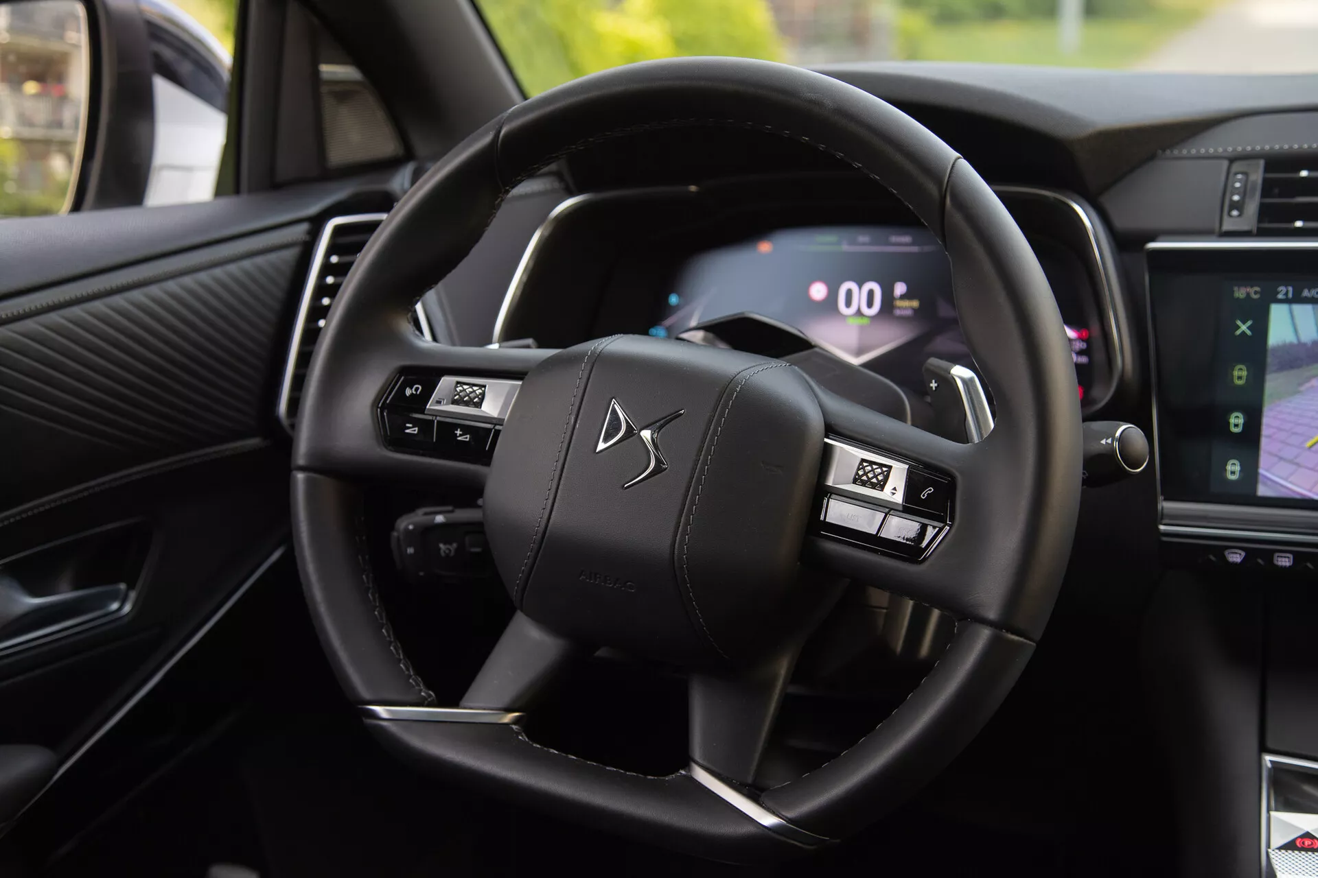 Interiérový pohľad na DS Automobiles DS-7 2022 zobrazujúci volant s multifunkčnými tlačidlami a digitálny prístrojový panel, vrátane pádiel radenia za volantom a časti systému infotainment zobrazujúce navigáciu
