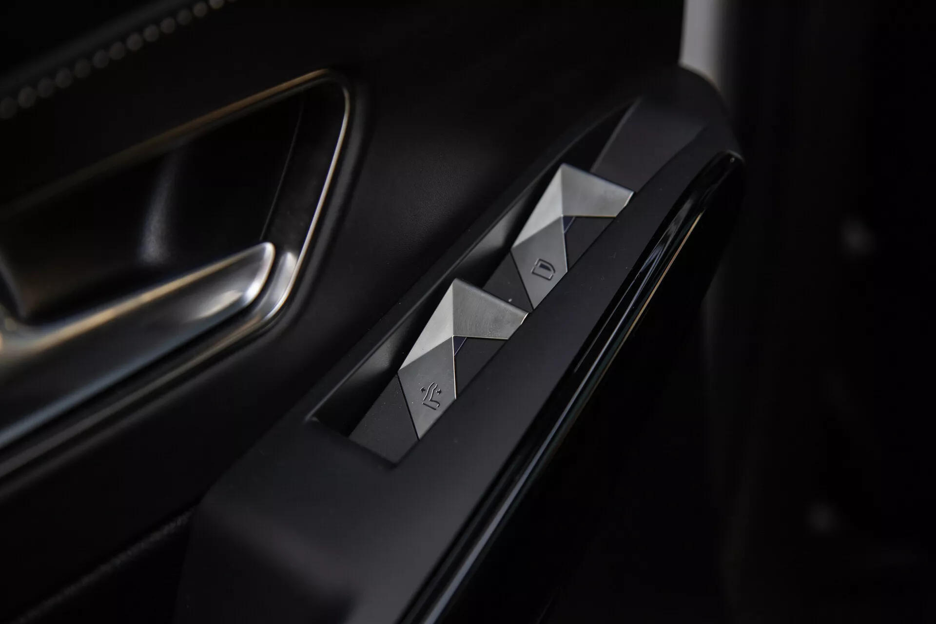 Detailný pohľad na ovládacie prvky na dverách vodiča auta DS Automobiles DS-7 2022 s prepínačmi okien s diamantovým strihom, tlačidlom zámku dverí, prémiovými matnými a kovovými povrchmi a sofistikovaným osvetlením zdôrazňujúcim ergonomický dizajn.