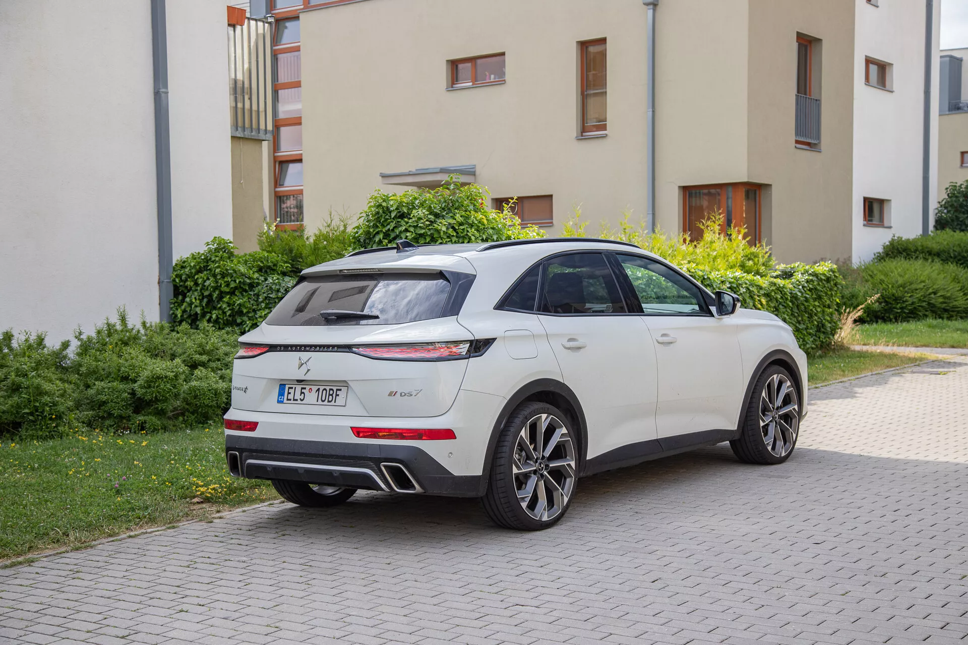 DS Automobiles DS-7 2022 zaparkované na príjazdovej ceste vedľa trávnatej plochy, zdôrazňujúce jeho zadný trojštvrťový pohľad s LED zadnými svetlami, zadným difúzorom, dvojitými výfukmi, strešným spojlerom, anténou v tvare plutvy žraloka a päťramennými zliatinovými kolesami.