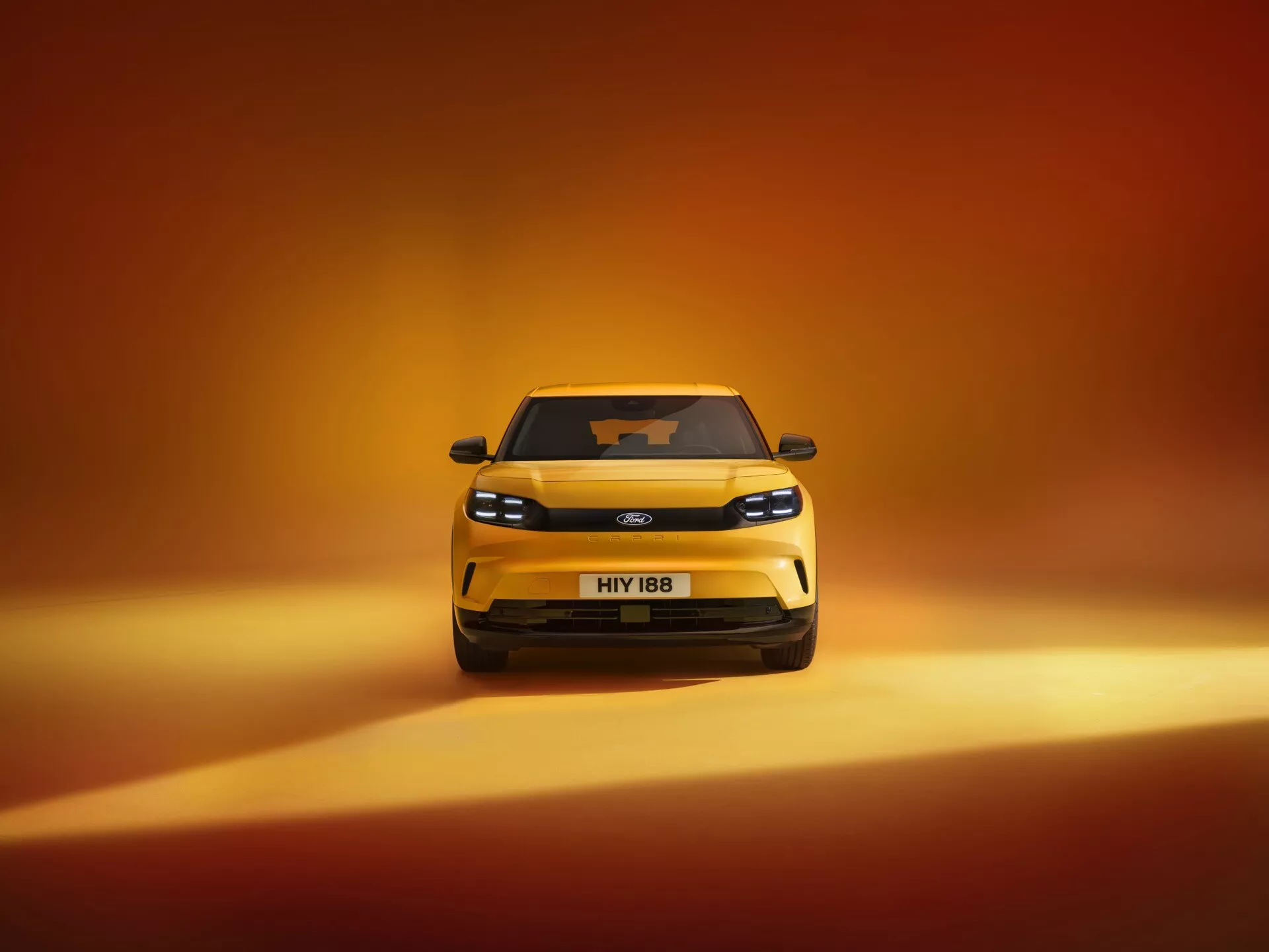 Predný pohľad na Ford Capri 2024 (4. generácia), moderný hatchback s LED svetlometmi, výraznou prednou mriežkou a elegantným dizajnom, zasadený proti gradientnému pozadiu prechádzajúcemu z tmavo oranžovej do svetlejšieho teplého odtieňa, zdôrazňujúc jeho dramatický a prémiový vzhľad v profesionálnej, vysoko kvalitnej fotografii.