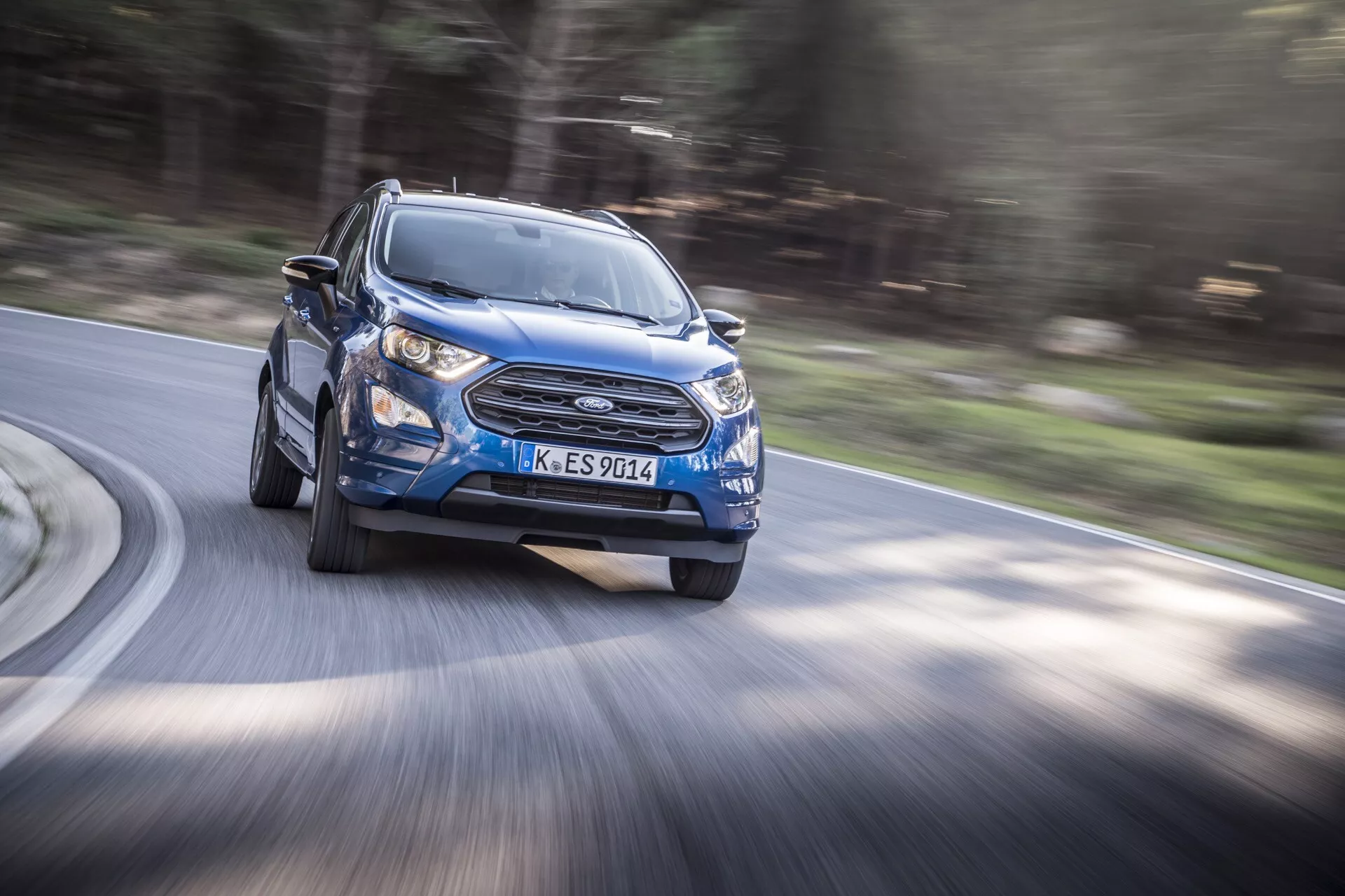 Ford EcoSport 2017 (1. generácia po facelifte) v dynamickej modrej farbe zachytávajúci pohyb z pohľadu z predného trojštvrtečného uhla, ktorý zdôrazňuje línie dizajnu, vzor mriežky a konfiguráciu LED svetlometov